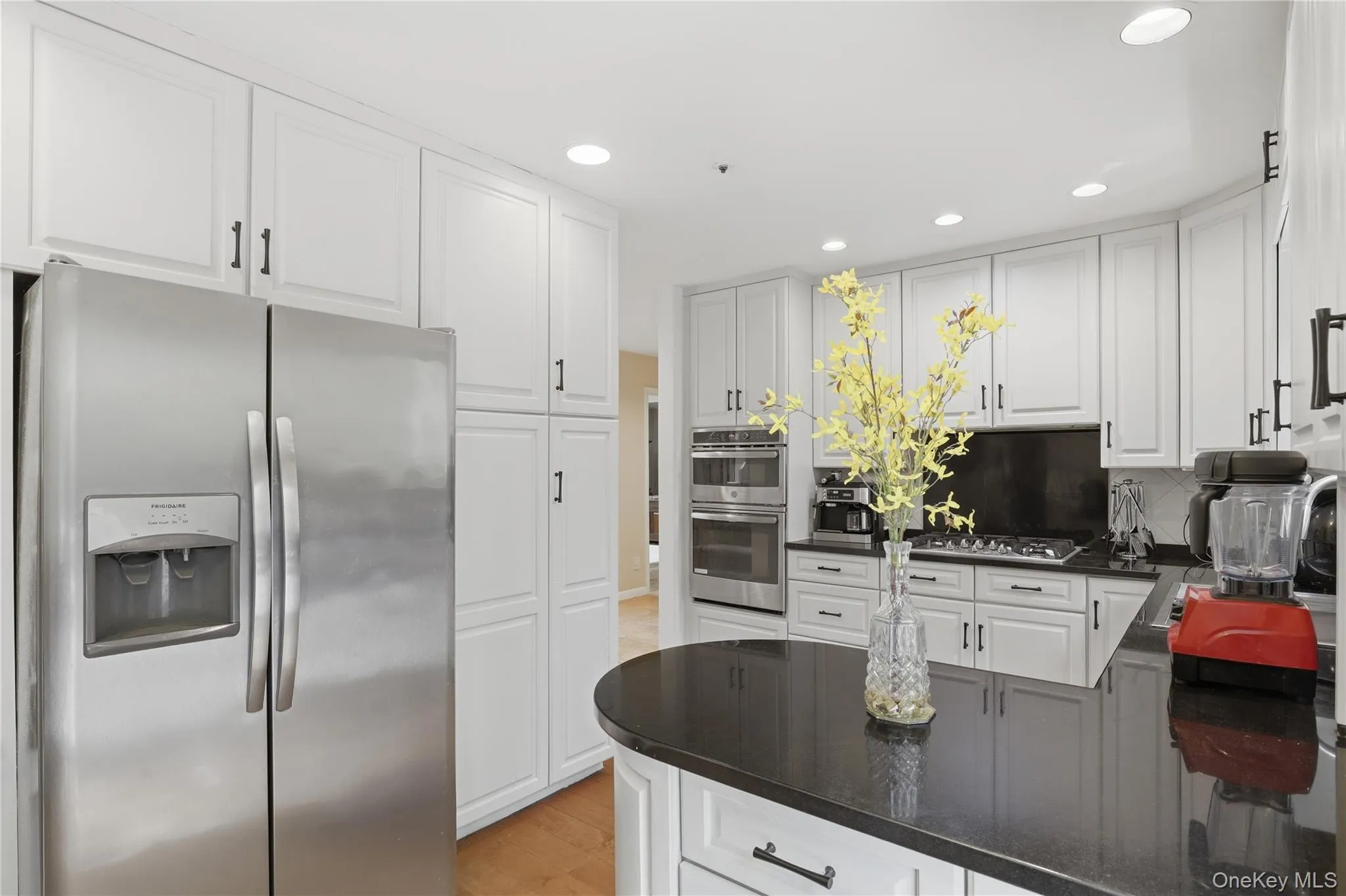 Modern kitchen featuring white cabinetry, dark countertops, recessed lighting, stainless steel side-by-side refrigerator, and built-in stainless steel double ovens Modern kitchen featuring white cabinetry, dark countertops, recessed lighting, stainless steel side-by-side refrigerator, and built-in stainless steel double ovens