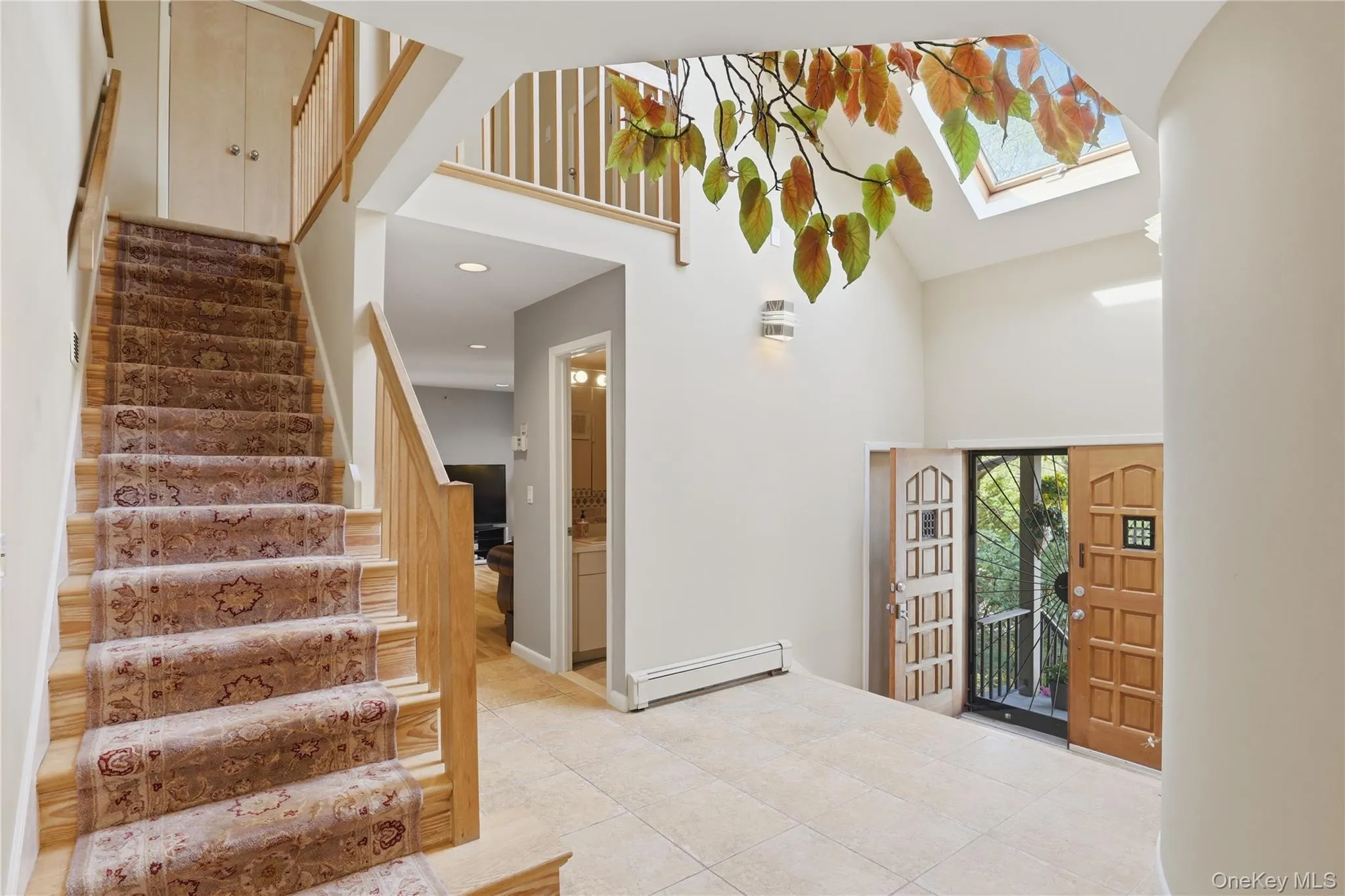 Two-story foyer featuring light-toned wood-finish entrance doors, tiled flooring, and a skylight Two-story foyer featuring light-toned wood-finish entrance doors, tiled flooring, and a skylight