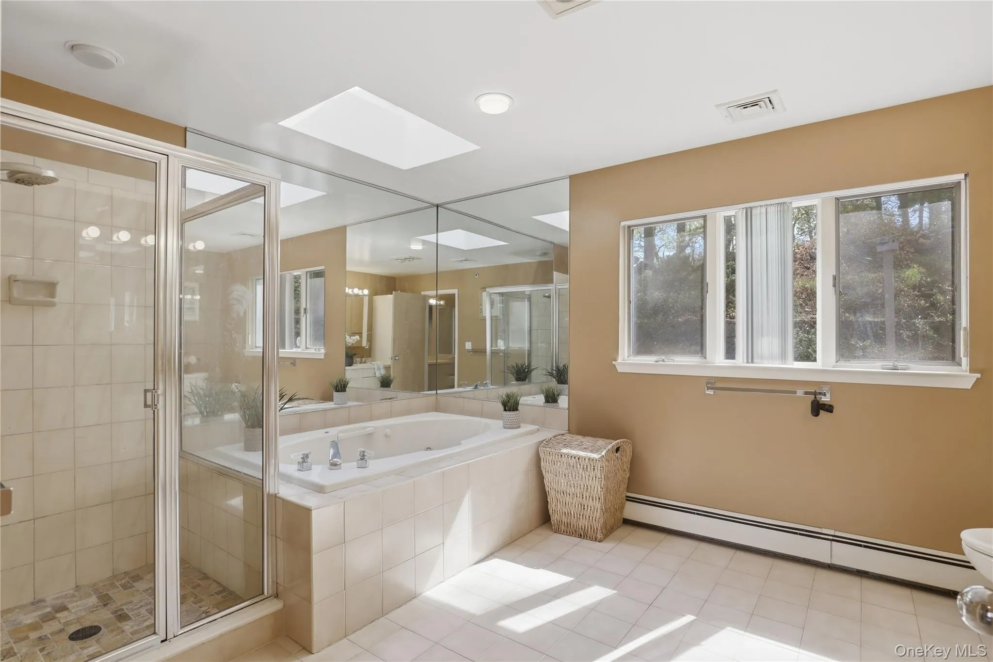 Primary Bathroom featuring a built-in jetted tub, a glass-enclosed shower with tiled walls, multiple windows, a ceiling-mounted skylight, and wall-to-wall mirrors Primary Bathroom featuring a built-in jetted tub, a glass-enclosed shower with tiled walls, multiple windows, a ceiling-mounted skylight, and wall-to-wall mirrors