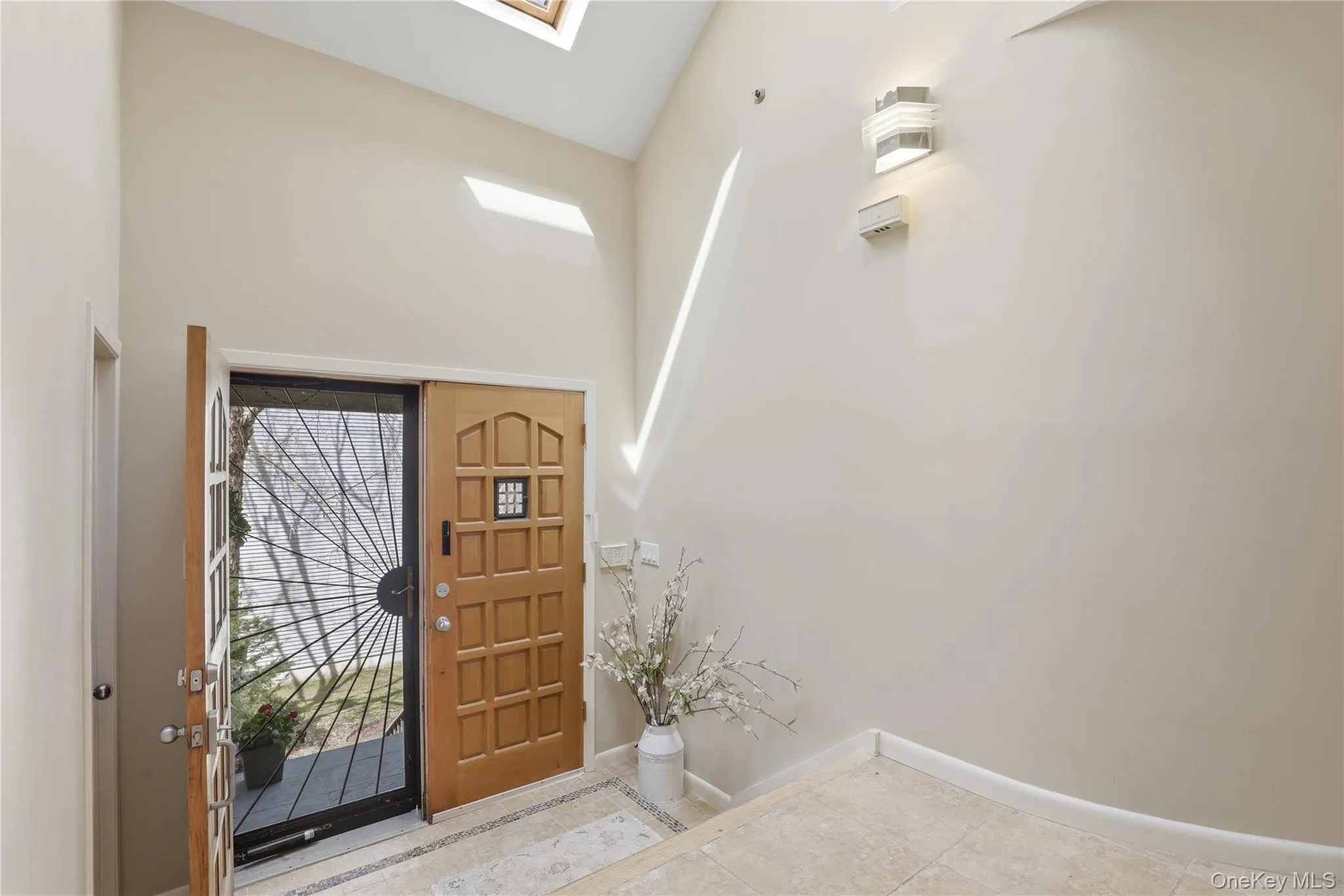 Entryway featuring a vaulted ceiling with skylights, light wood-finish door with security screen, and tile flooring with decorative inlay Entryway featuring a vaulted ceiling with skylights, light wood-finish door with security screen, and tile flooring with decorative inlay