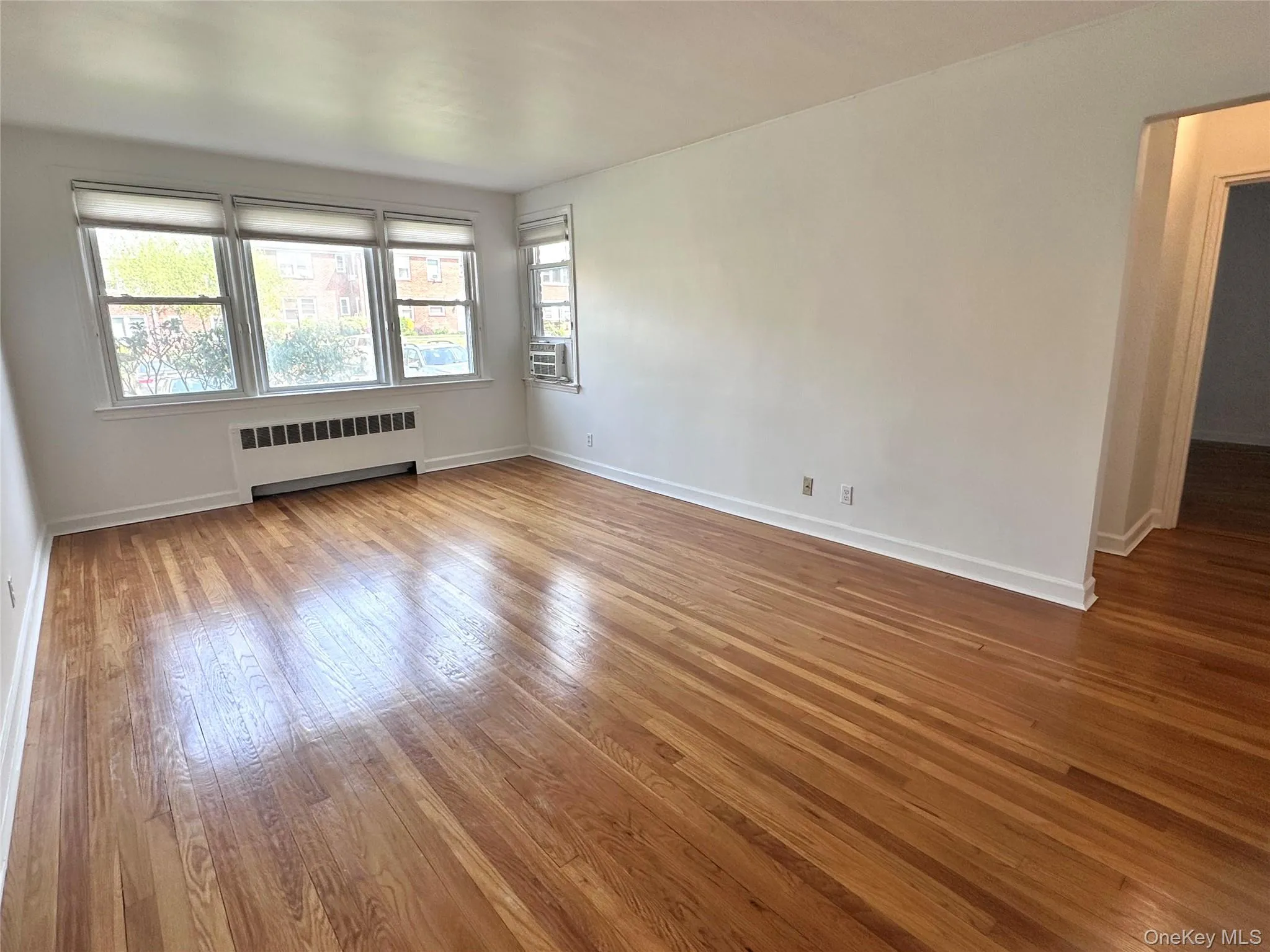 Spacious room featuring wood flooring, white baseboards, and multiple windows with roller shades; AC included Spacious room featuring wood flooring, white baseboards, and multiple windows with roller shades; AC included