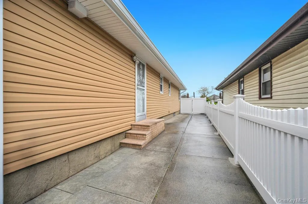 Side exterior showcasing tan horizontal siding, a concrete pathway, a privacy fence, and brick steps leading to an entry door with a security screen Side exterior showcasing tan horizontal siding, a concrete pathway, a privacy fence, and brick steps leading to an entry door with a security screen