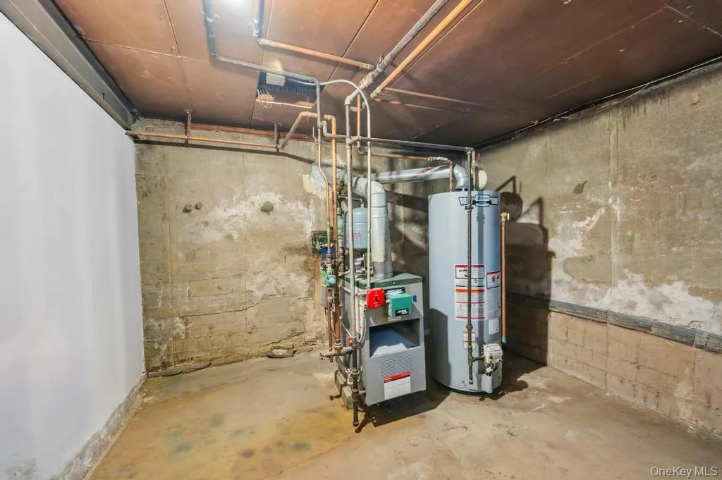 Utility space featuring a water heater, boiler system, and visible copper piping Utility space featuring a water heater, boiler system, and visible copper piping