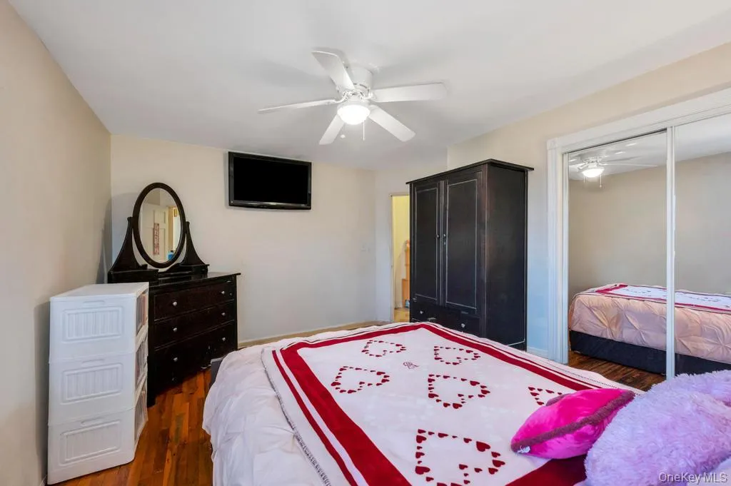 Bedroom featuring wood-finish flooring, a ceiling fan with integrated lighting, and a mirrored sliding closet door Bedroom featuring wood-finish flooring, a ceiling fan with integrated lighting, and a mirrored sliding closet door