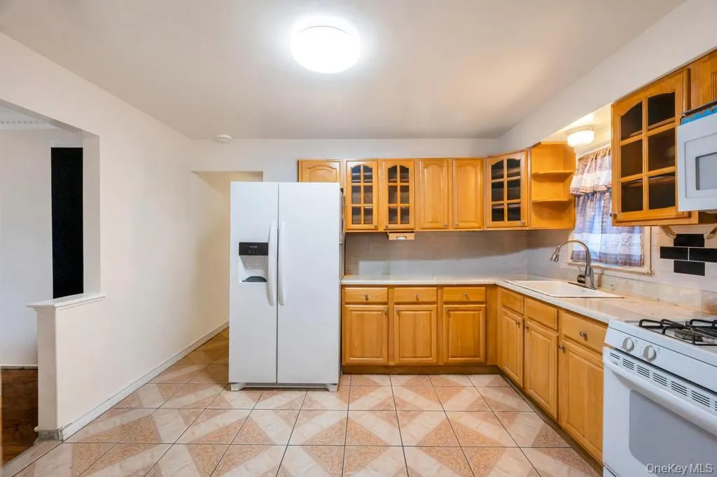 Kitchen featuring wood cabinetry, light-toned countertops, a white side-by-side refrigerator, and patterned tile flooring Kitchen featuring wood cabinetry, light-toned countertops, a white side-by-side refrigerator, and patterned tile flooring