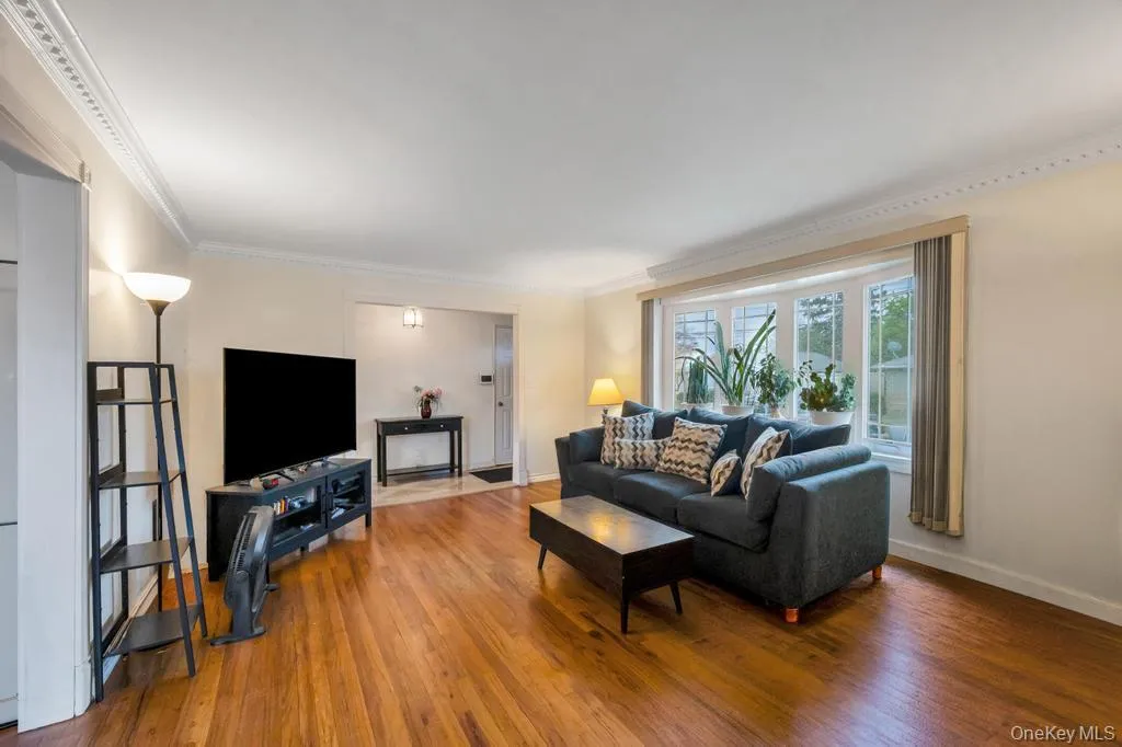 Living area featuring wood-finish flooring, a bay window with multiple panes, crown molding, and a neutral wall color Living area featuring wood-finish flooring, a bay window with multiple panes, crown molding, and a neutral wall color