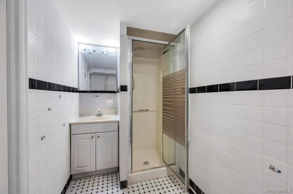 Bathroom featuring a glass-enclosed shower, a white vanity with a built-in sink, and a mirrored medicine cabinet with integrated lighting Bathroom featuring a glass-enclosed shower, a white vanity with a built-in sink, and a mirrored medicine cabinet with integrated lighting