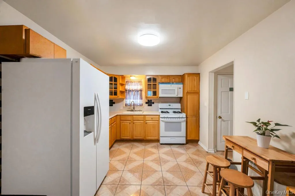 Kitchen featuring wood cabinetry, white appliances, a patterned tile floor, and a tile backsplash Kitchen featuring wood cabinetry, white appliances, a patterned tile floor, and a tile backsplash