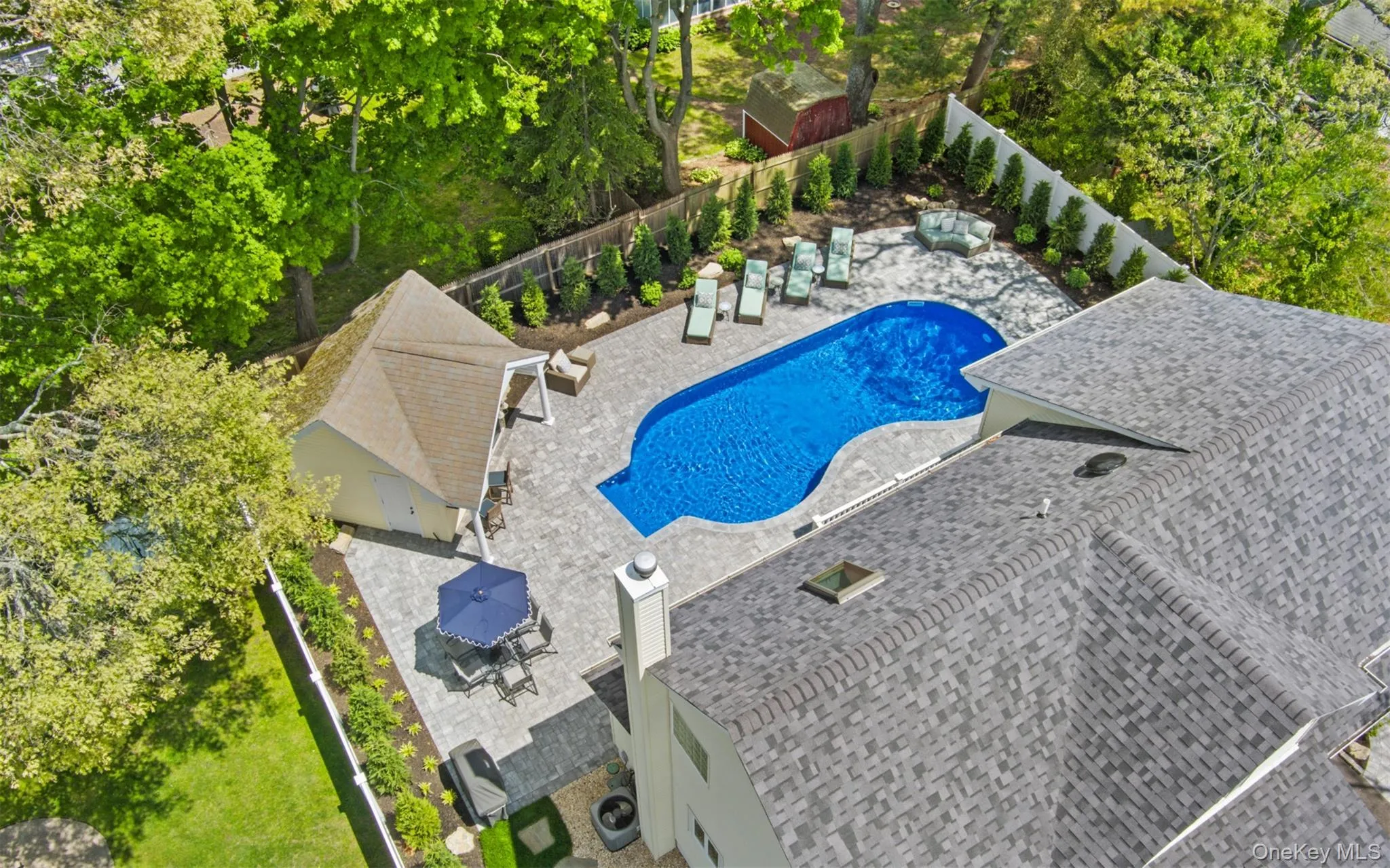 Free form swimming pool surrounded by a large paver patio, a freestanding pool house with a hip roof, and structured plantings Free form swimming pool surrounded by a large paver patio, a freestanding pool house with a hip roof, and structured plantings