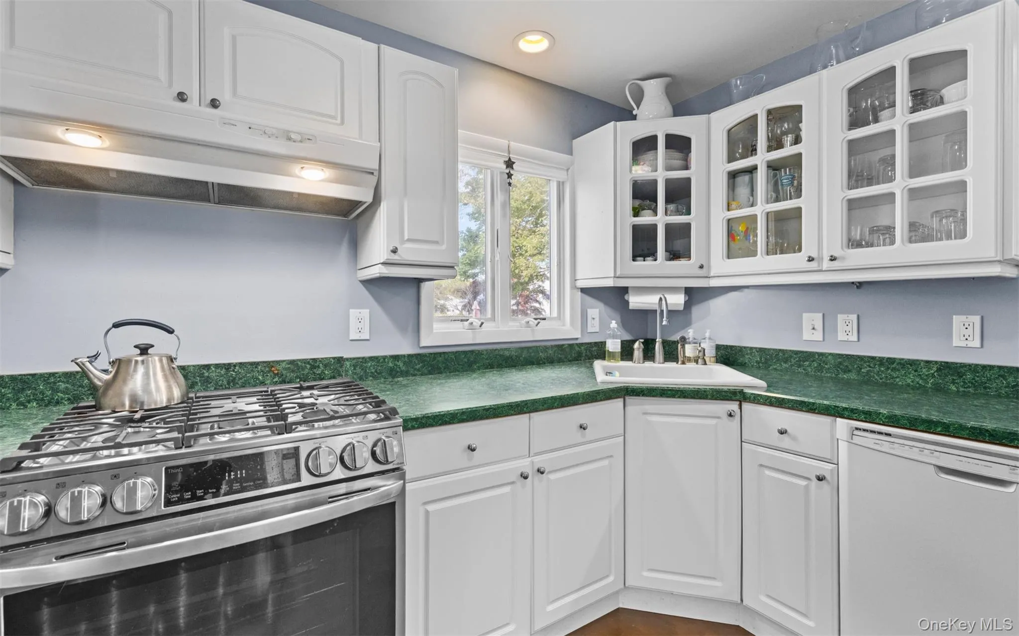 Kitchen featuring white cabinetry, formica countertops, stainless steel gas range, and a corner sink with window Kitchen featuring white cabinetry, formica countertops, stainless steel gas range, and a corner sink with window