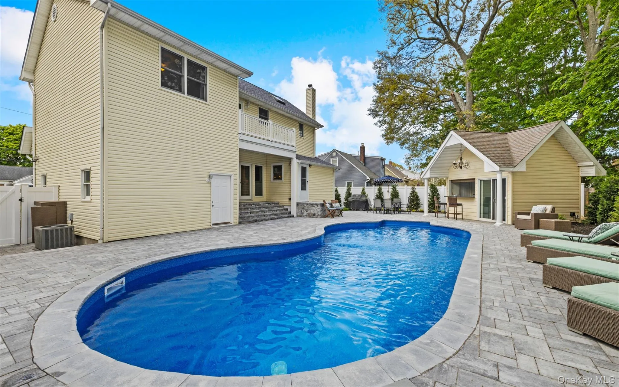 Free form in-ground swimming pool surrounded by extensive paver patio, featuring a dedicated pool house with an outdoor bar Free form in-ground swimming pool surrounded by extensive paver patio, featuring a dedicated pool house with an outdoor bar