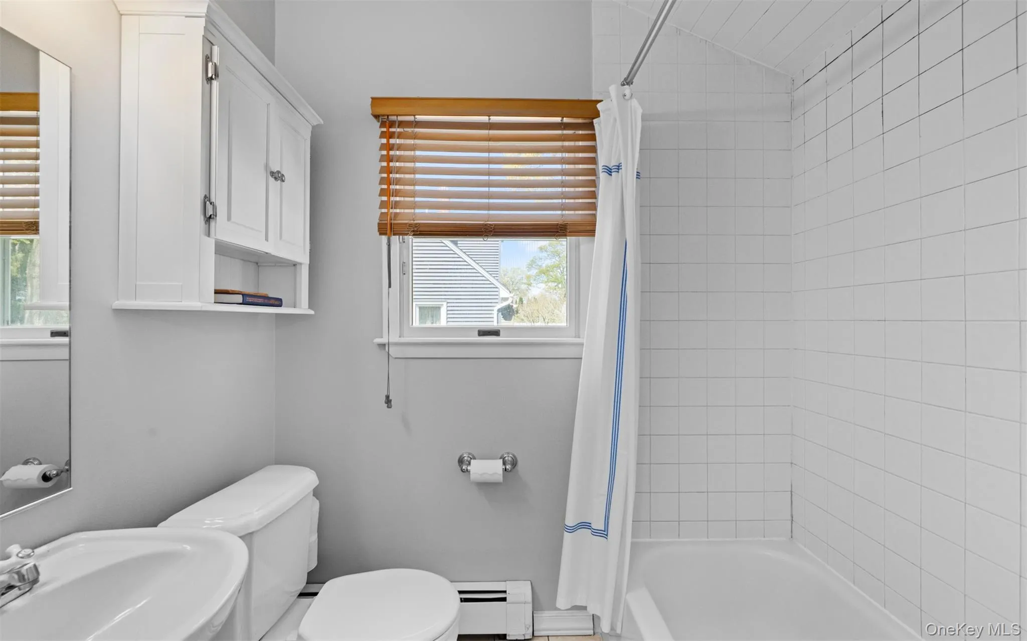 First floor full bathroom featuring a tiled shower-over-tub, a white toilet, and a window with wood-finish blinds First floor full bathroom featuring a tiled shower-over-tub, a white toilet, and a window with wood-finish blinds