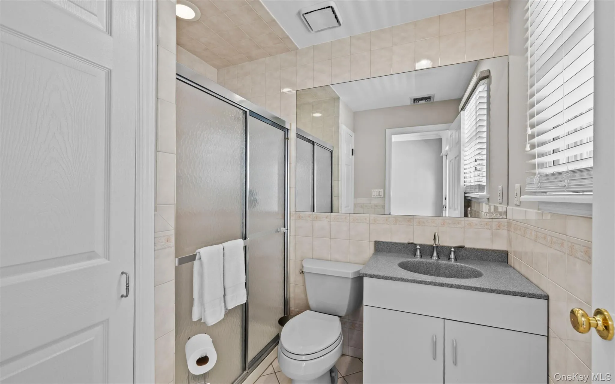 Second floor guest bathroom featuring a sliding glass shower enclosure, a vanity with an integrated sink and base cabinetry, a wall-mounted mirror, and tile flooring Second floor guest bathroom featuring a sliding glass shower enclosure, a vanity with an integrated sink and base cabinetry, a wall-mounted mirror, and tile flooring
