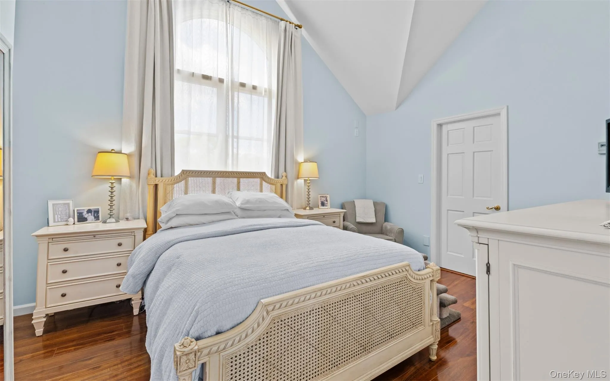 This room features a high vaulted cathedral ceiling, dark wood flooring, and a tall arched window with sheer and blackout drapery This room features a high vaulted cathedral ceiling, dark wood flooring, and a tall arched window with sheer and blackout drapery