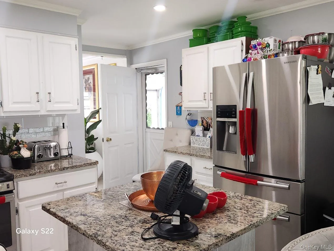 Kitchen with stainless steel fridge with ice dispenser, white cabinetry, ornamental molding, a kitchen island, and light stone counters Kitchen with stainless steel fridge with ice dispenser, white cabinetry, ornamental molding, a kitchen island, and light stone counters