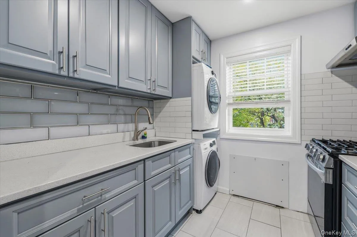 Kitchen featuring grey shaker-style cabinetry with brushed nickel hardware, light-toned countertops, and a subway tile backsplash Kitchen featuring grey shaker-style cabinetry with brushed nickel hardware, light-toned countertops, and a subway tile backsplash