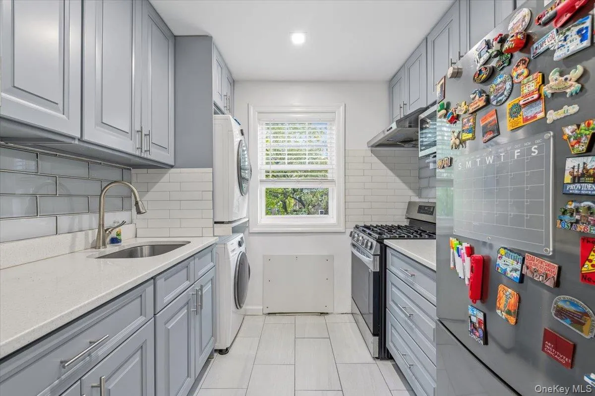 Galley kitchen with light gray cabinetry, white subway tile backsplash, and light-toned countertops Galley kitchen with light gray cabinetry, white subway tile backsplash, and light-toned countertops