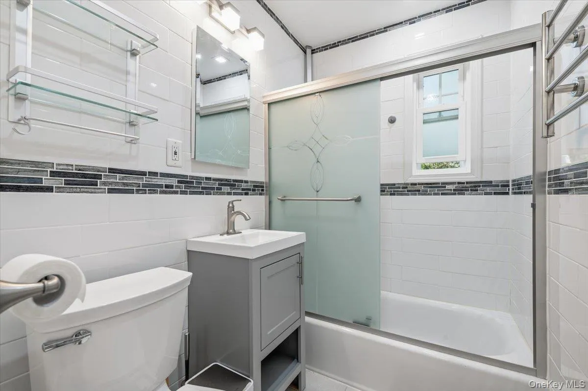 Bathroom featuring white subway tile, a decorative glass mosaic accent band, and a sliding glass shower door with etched detailing Bathroom featuring white subway tile, a decorative glass mosaic accent band, and a sliding glass shower door with etched detailing