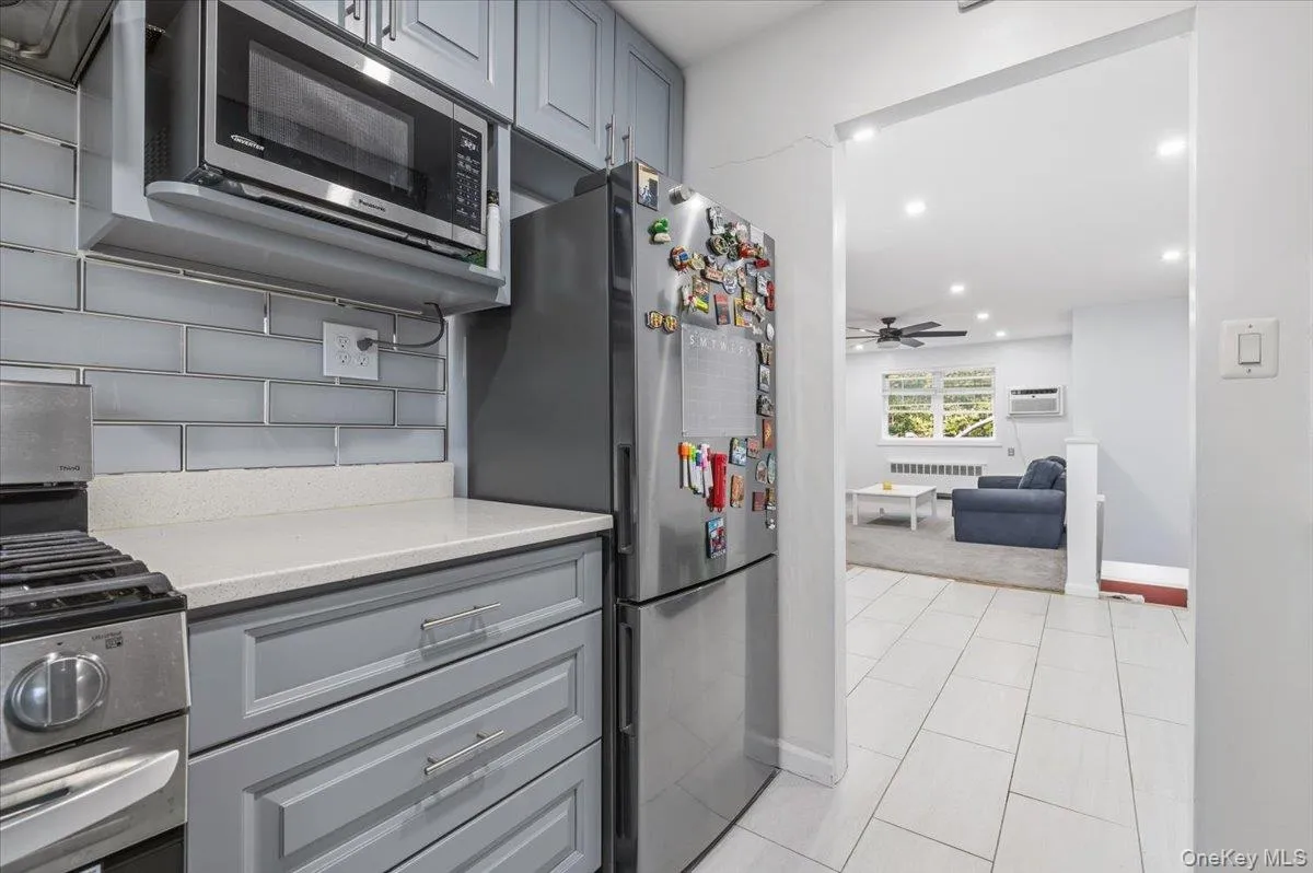 Kitchen featuring light gray cabinetry, stainless steel appliances, a white solid surface countertop, and a gray subway tile backsplash Kitchen featuring light gray cabinetry, stainless steel appliances, a white solid surface countertop, and a gray subway tile backsplash