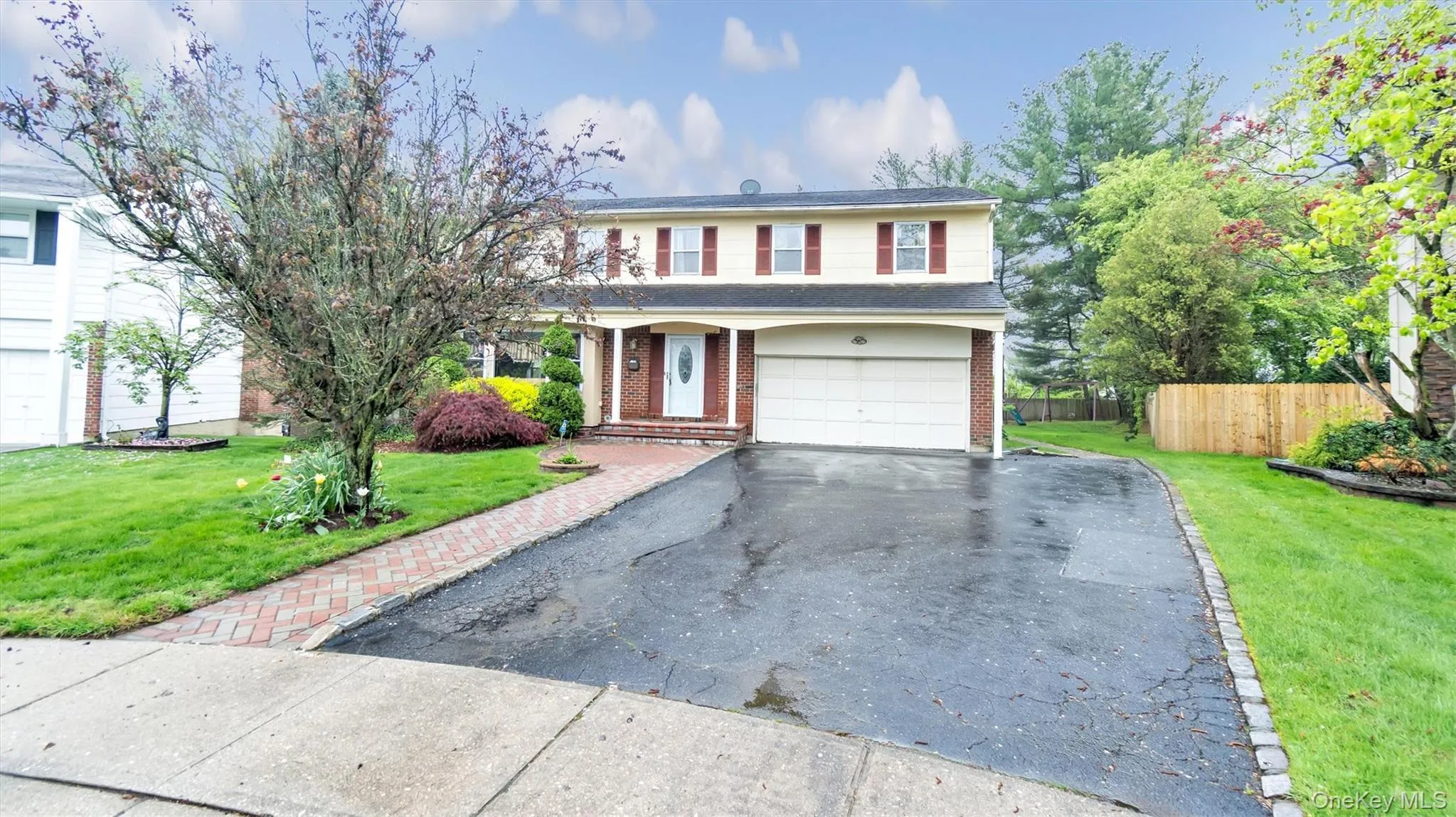 Traditional-style home featuring a garage, fence, aphalt driveway, a front yard, and brick siding Traditional-style home featuring a garage, fence, aphalt driveway, a front yard, and brick siding