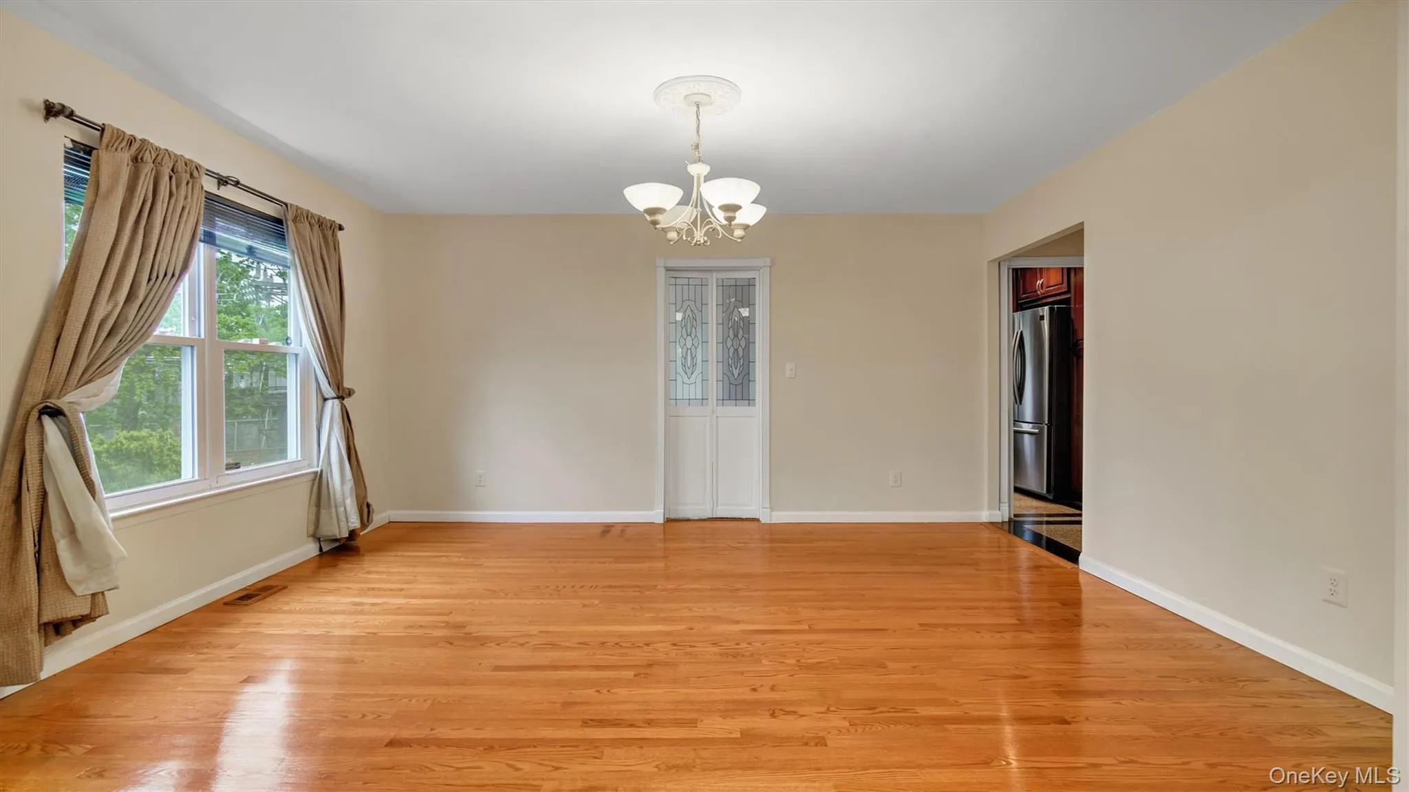 Spare room featuring an inviting chandelier, baseboards, visible vents, and light wood-style floors Spare room featuring an inviting chandelier, baseboards, visible vents, and light wood-style floors