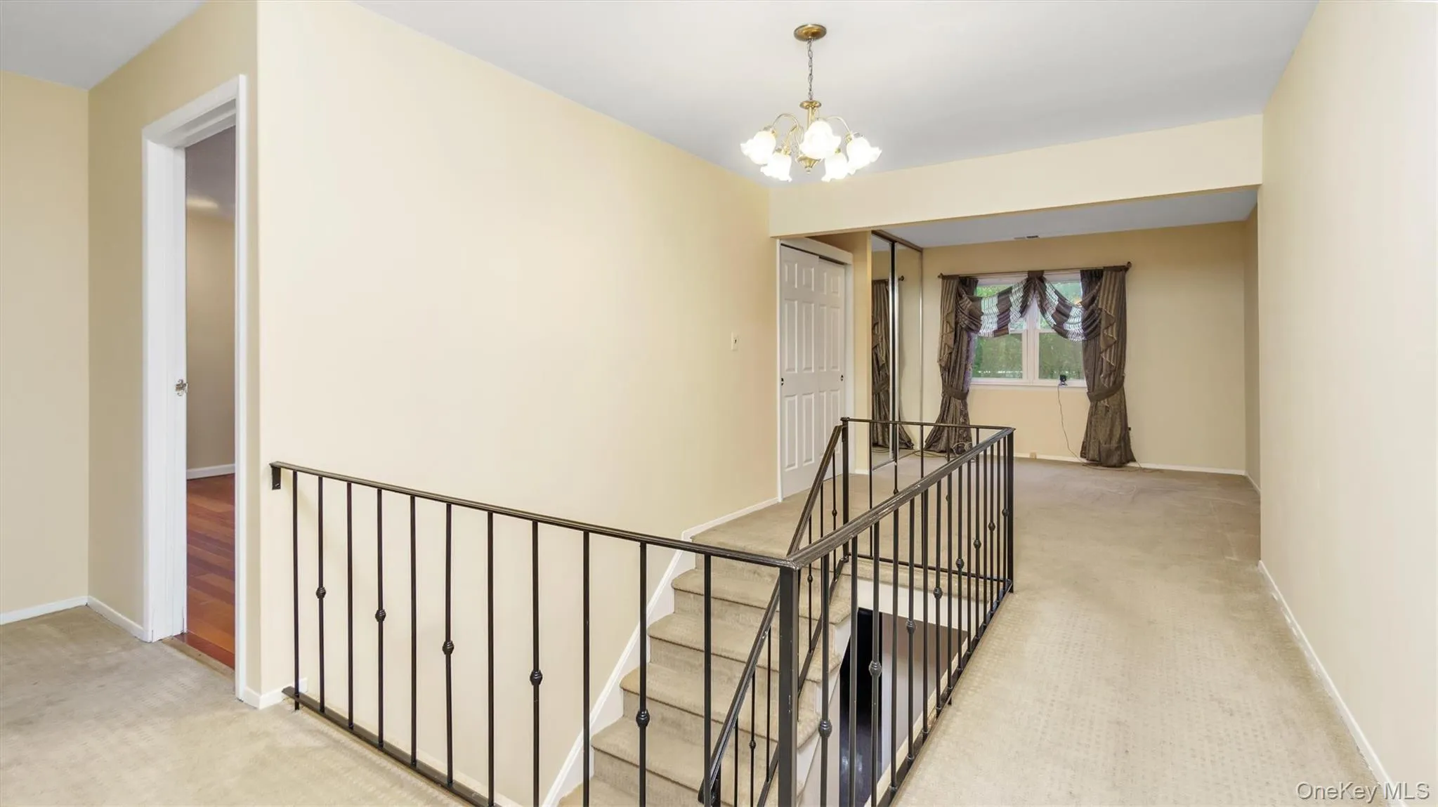 Hallway featuring baseboards, light carpet, an upstairs landing, and a chandelier Hallway featuring baseboards, light carpet, an upstairs landing, and a chandelier
