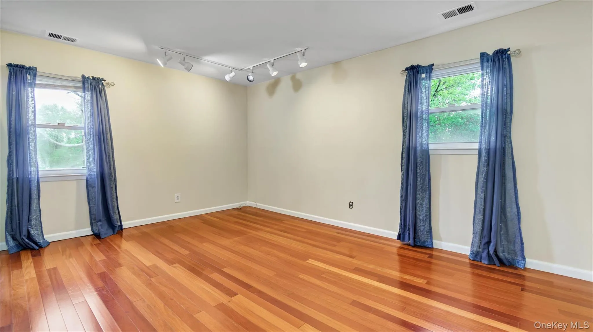 Empty room with rail lighting, light wood-style floors, visible vents, and baseboards Empty room with rail lighting, light wood-style floors, visible vents, and baseboards