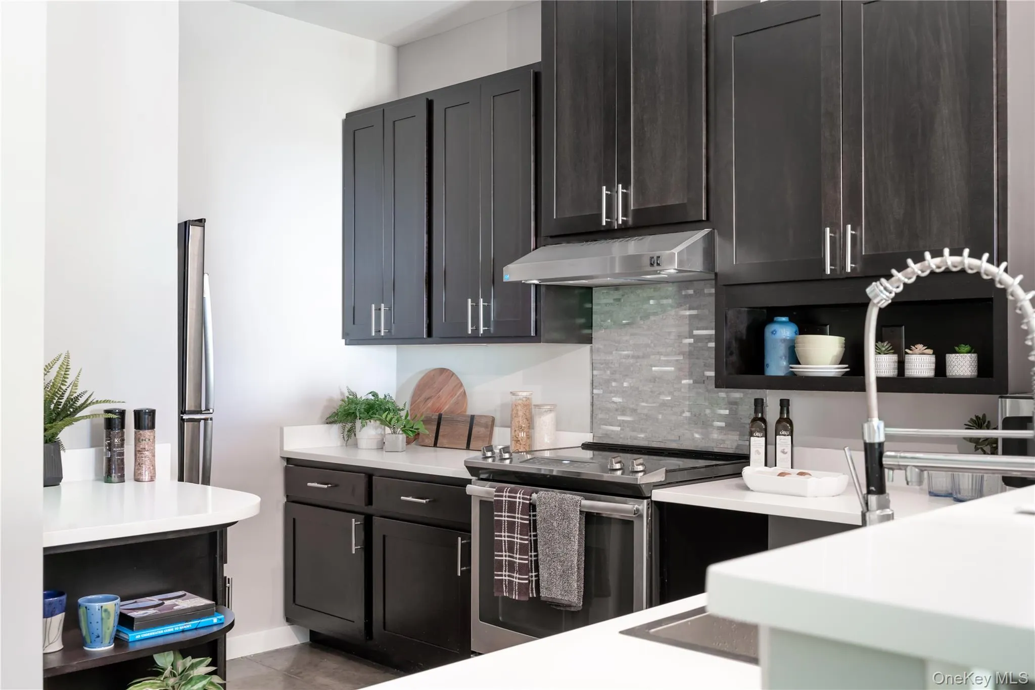 The kitchen features dark cabinetry with silver hardware, quartz countertops, and stainless-steel appliances The kitchen features dark cabinetry with silver hardware, quartz countertops, and stainless-steel appliances