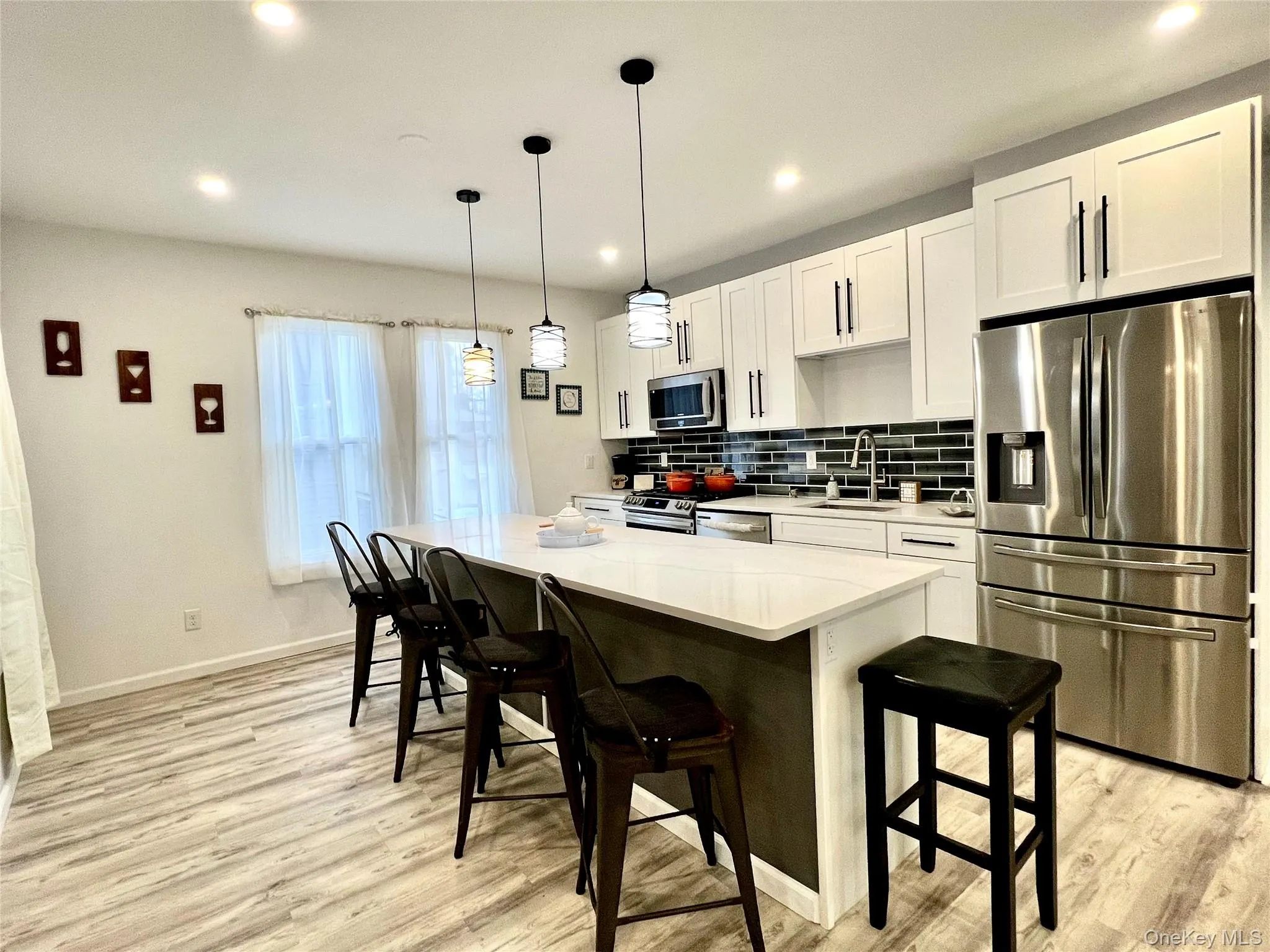 Kitchen featuring appliances with stainless steel finishes, white cabinetry, tasteful backsplash, a breakfast bar area, and hanging light fixtures Kitchen featuring appliances with stainless steel finishes, white cabinetry, tasteful backsplash, a breakfast bar area, and hanging light fixtures