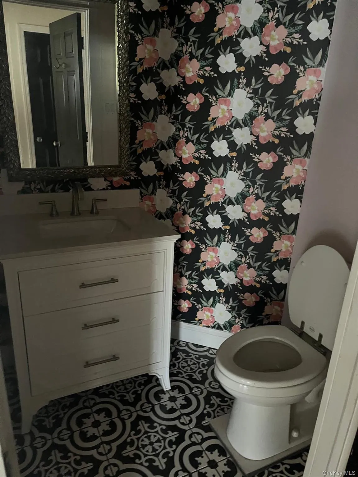 Powder room featuring black and white patterned floor tiles, a white vanity with drawers, and a floral-patterned accent wall Powder room featuring black and white patterned floor tiles, a white vanity with drawers, and a floral-patterned accent wall
