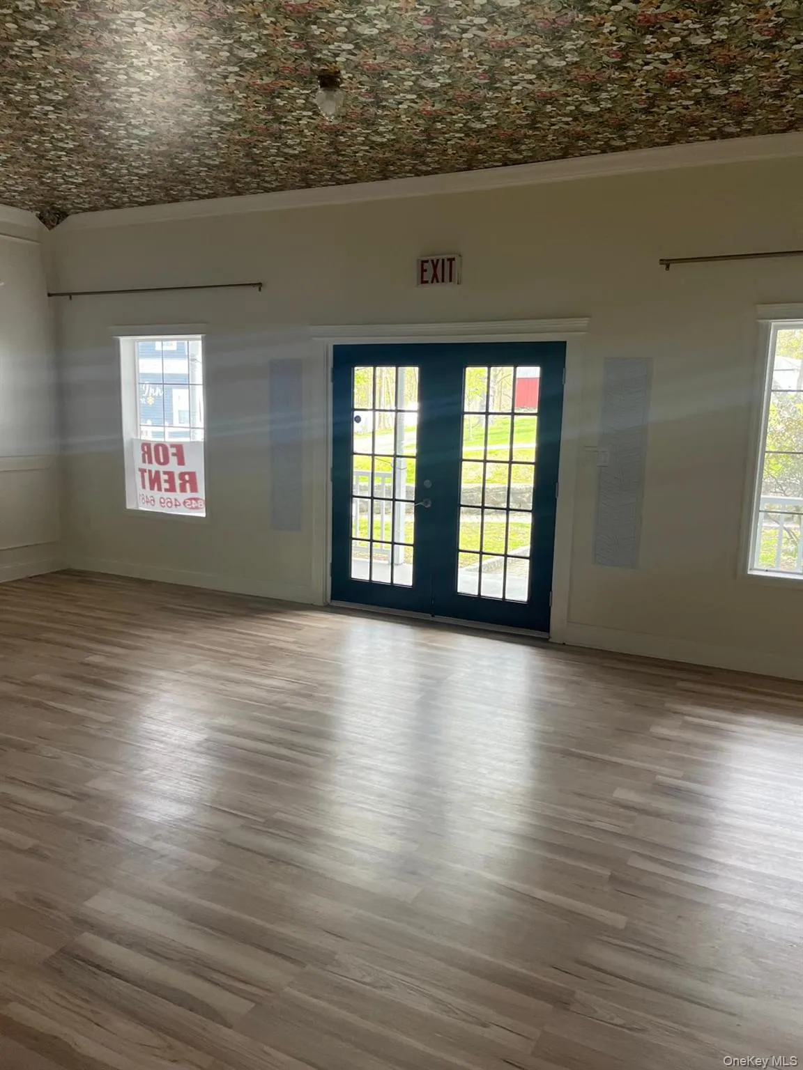 Spacious room featuring wood-finish flooring, light-toned walls, and a patterned ceiling Spacious room featuring wood-finish flooring, light-toned walls, and a patterned ceiling