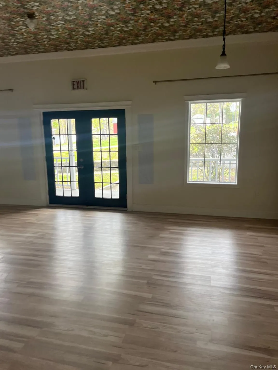 Spacious room featuring wood-finish flooring, light-colored walls, and a patterned ceiling Spacious room featuring wood-finish flooring, light-colored walls, and a patterned ceiling