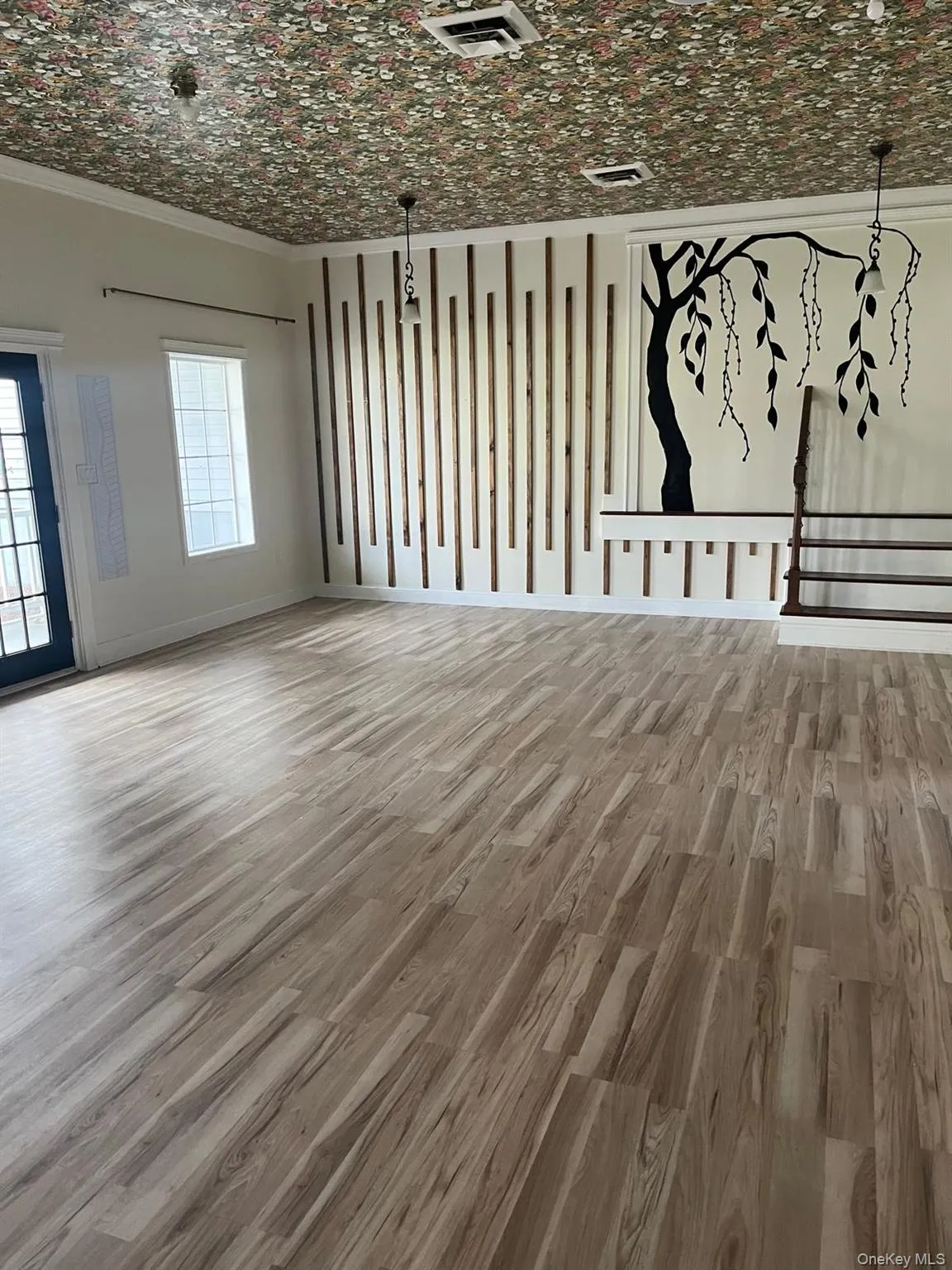 Spacious room featuring wood-finish flooring, a decorative floral ceiling, and a wall accent of vertical wood slats with a tree mural Spacious room featuring wood-finish flooring, a decorative floral ceiling, and a wall accent of vertical wood slats with a tree mural