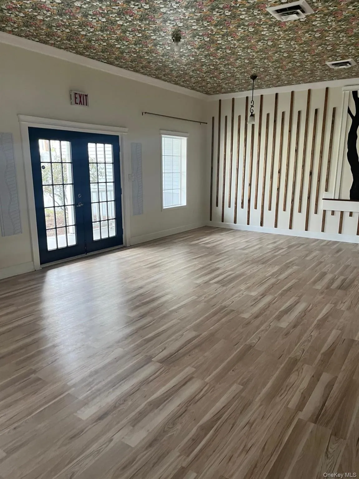 Spacious room featuring wood-finish flooring, a floral patterned ceiling, and a decorative accent wall with vertical wood paneling Spacious room featuring wood-finish flooring, a floral patterned ceiling, and a decorative accent wall with vertical wood paneling