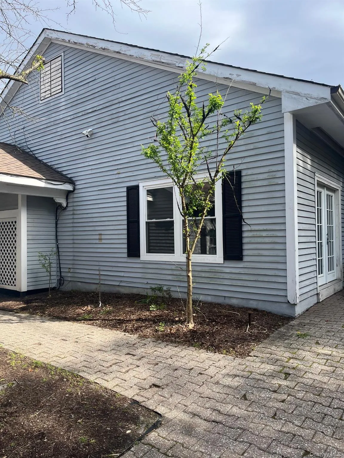 Exterior siding with a window featuring dark shutters, a small tree, and a paver pathway Exterior siding with a window featuring dark shutters, a small tree, and a paver pathway
