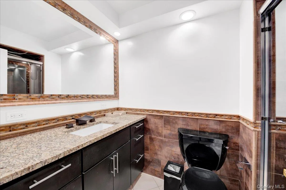 Full bath featuring a shower stall, vanity, tile walls, and wainscoting Full bath featuring a shower stall, vanity, tile walls, and wainscoting