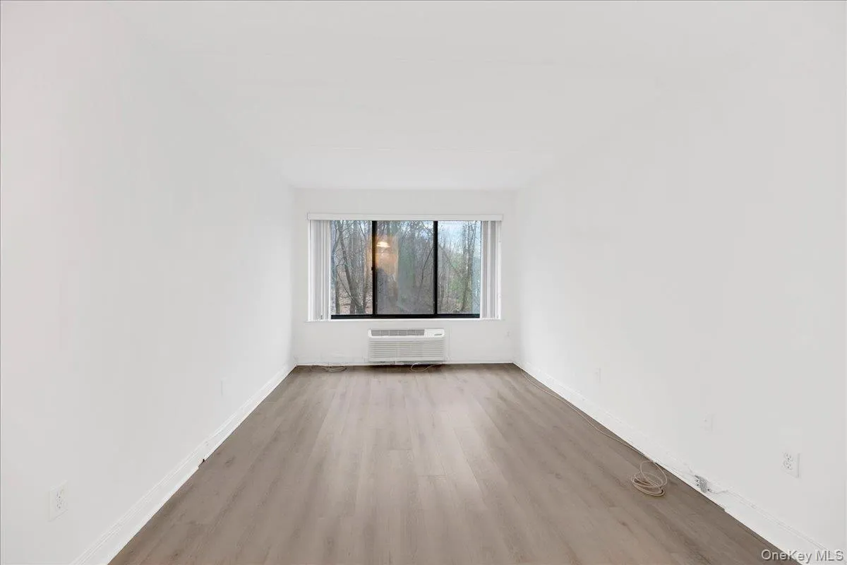 Unfurnished 2nd bedroom featuring a packaged terminal HVAC unit and wood finished floors Unfurnished 2nd bedroom featuring a packaged terminal HVAC unit and wood finished floors