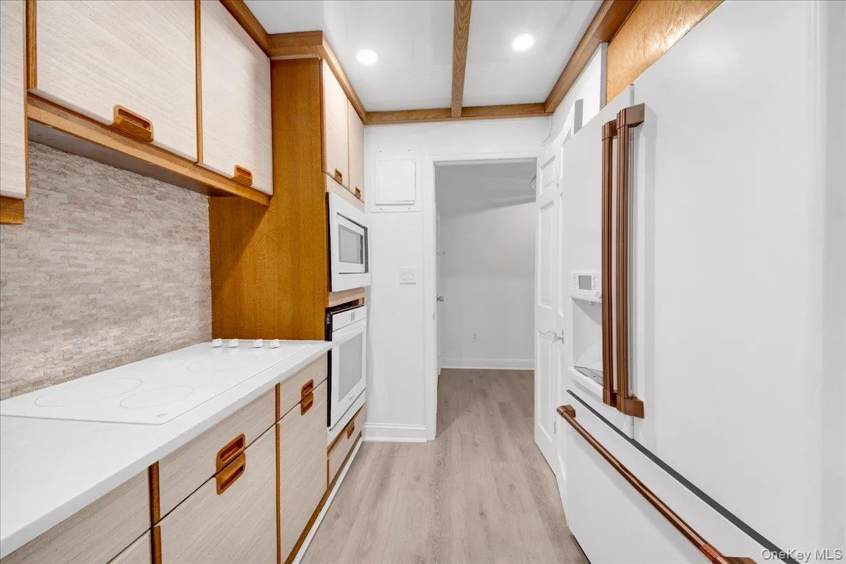 Two tone kitchen featuring white stainless steel appliances, light countertops, light wood-style flooring, dual tone cabinets, and recessed lighting Two tone kitchen featuring white stainless steel appliances, light countertops, light wood-style flooring, dual tone cabinets, and recessed lighting