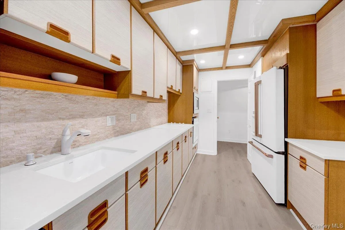 Kitchen with light wood finished floors, high end white stainless steel refrigerator, coffered ceiling, recessed lighting, and open shelves Kitchen with light wood finished floors, high end white stainless steel refrigerator, coffered ceiling, recessed lighting, and open shelves