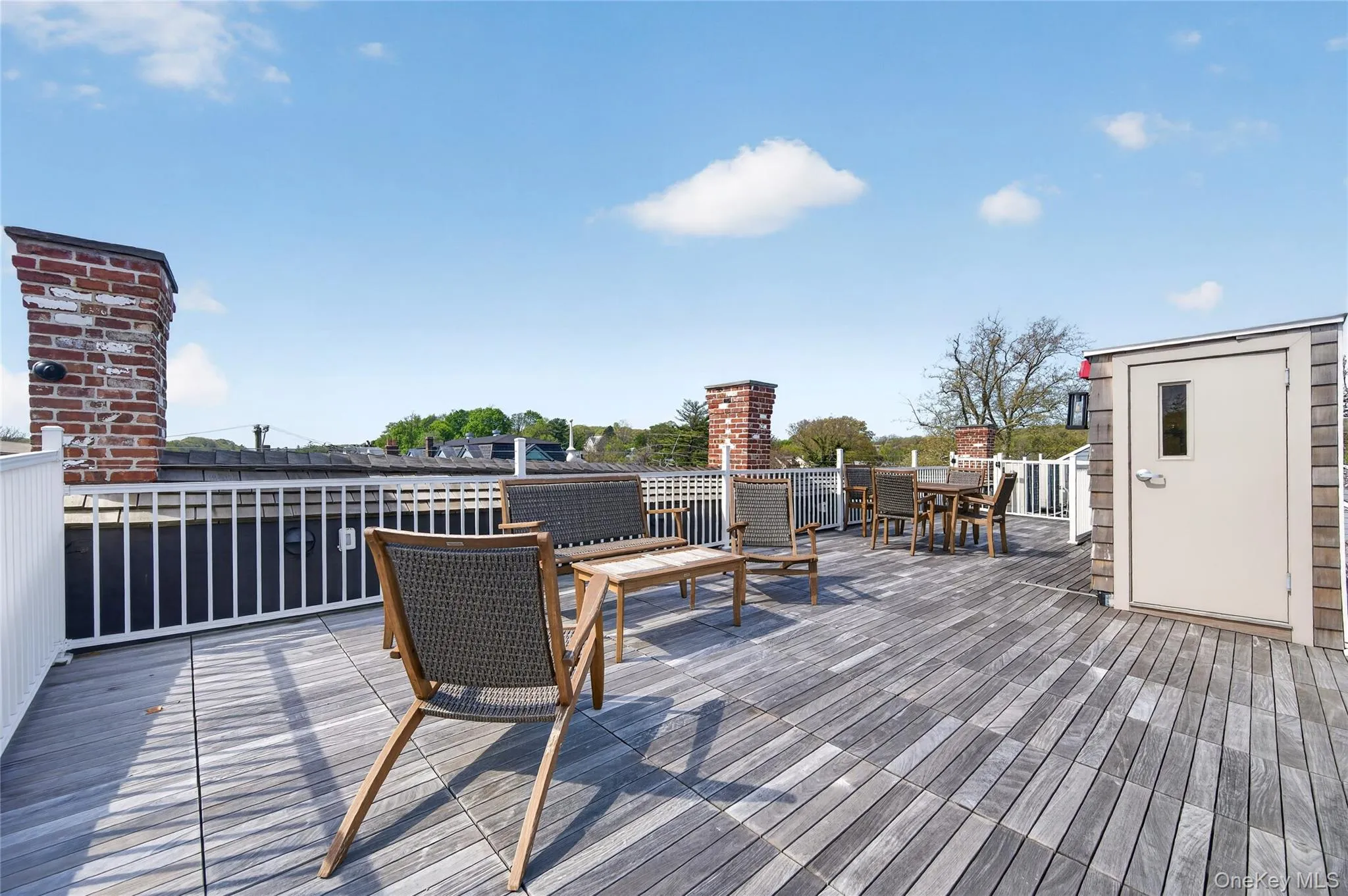 Expansive rooftop deck featuring a weathered wood-finish surface, white perimeter railings, brick chimneys, and a shingled storage shed Expansive rooftop deck featuring a weathered wood-finish surface, white perimeter railings, brick chimneys, and a shingled storage shed
