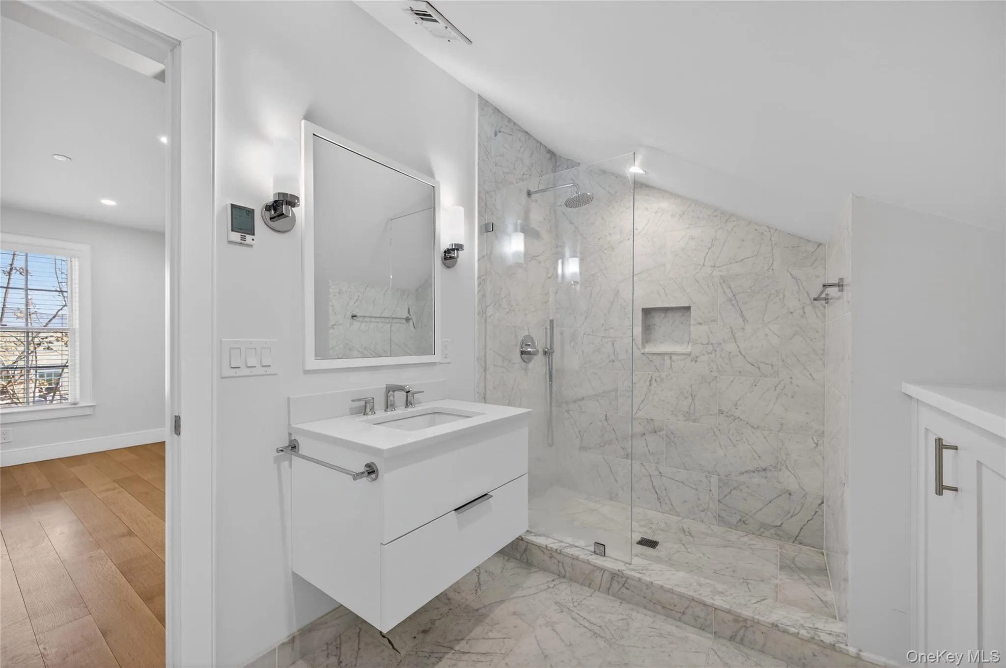 Bathroom featuring a floating vanity with a white countertop, a walk-in shower with clear glass enclosure, marble-style wall and floor tiling, and polished chrome fixtures Bathroom featuring a floating vanity with a white countertop, a walk-in shower with clear glass enclosure, marble-style wall and floor tiling, and polished chrome fixtures