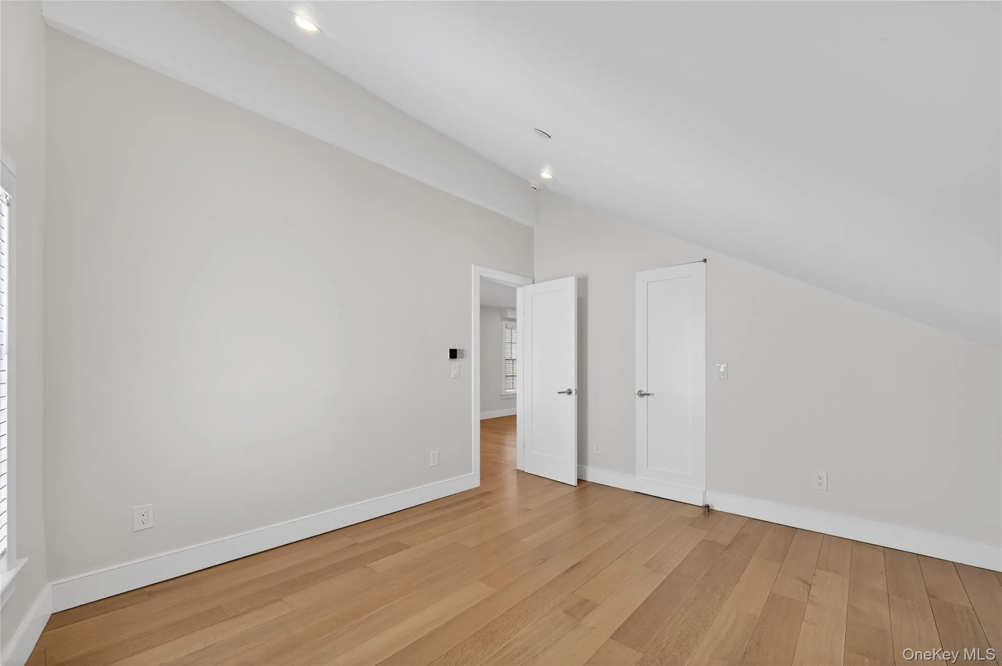 Spacious room featuring vaulted ceilings, light wood-finish flooring, recessed lighting, white baseboards, and interior doors with contemporary hardware Spacious room featuring vaulted ceilings, light wood-finish flooring, recessed lighting, white baseboards, and interior doors with contemporary hardware