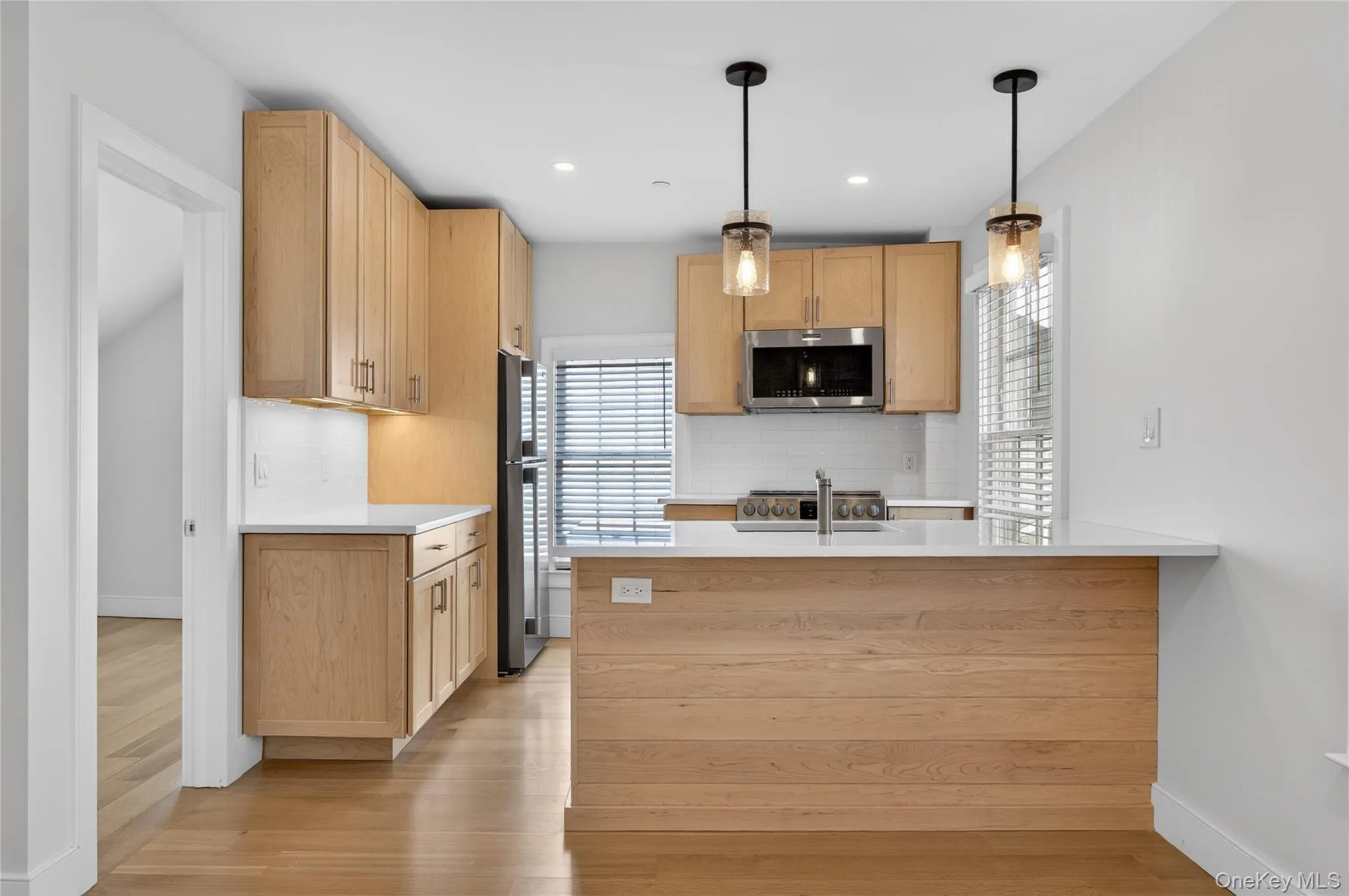 Modern kitchen featuring natural wood cabinetry, stainless steel appliances, white quartz countertops, and a subway tile backsplash Modern kitchen featuring natural wood cabinetry, stainless steel appliances, white quartz countertops, and a subway tile backsplash