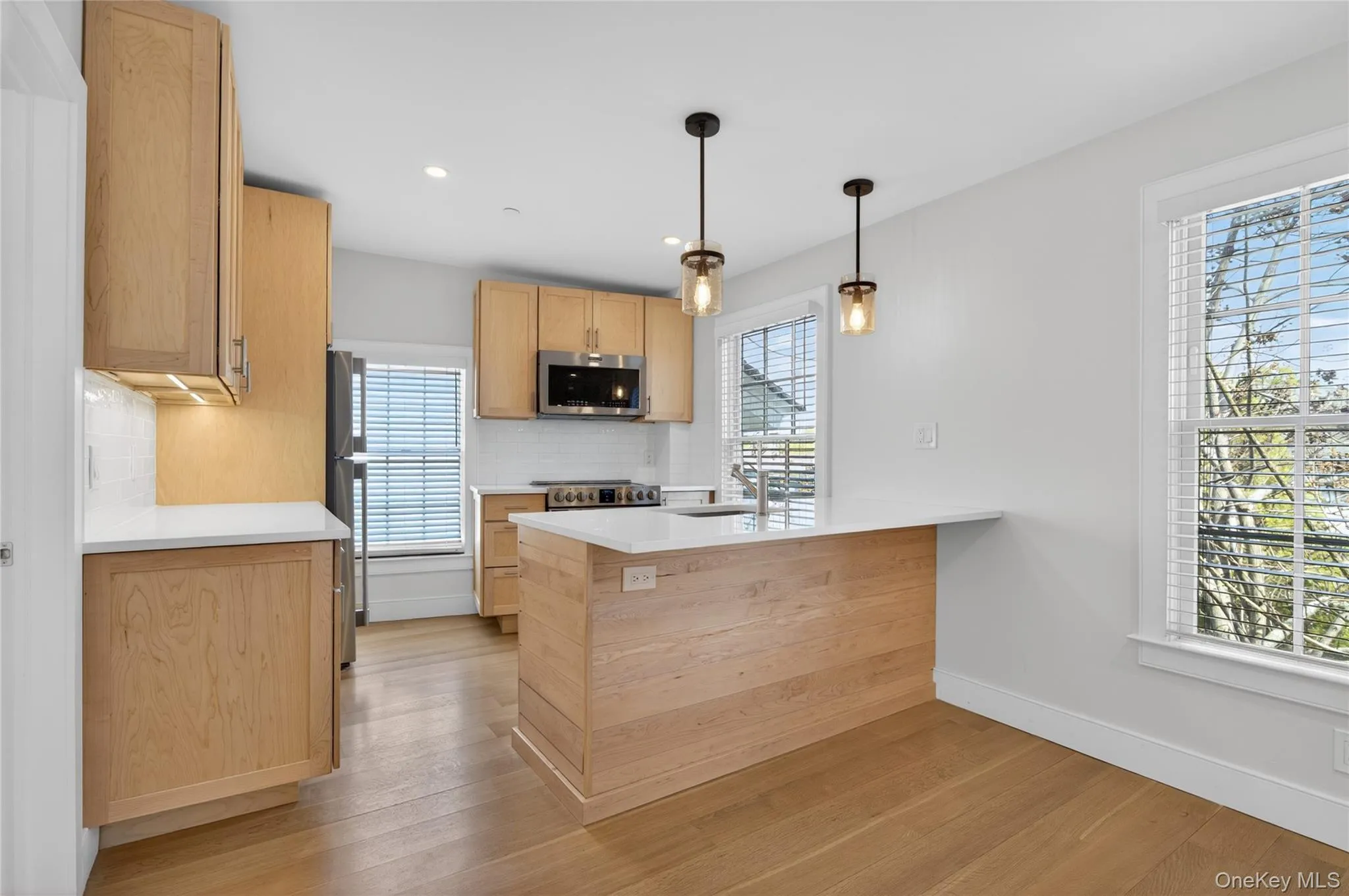 Open-concept kitchen featuring wood-finish flooring, light wood cabinetry, white quartz countertops, and a subway tile backsplash Open-concept kitchen featuring wood-finish flooring, light wood cabinetry, white quartz countertops, and a subway tile backsplash