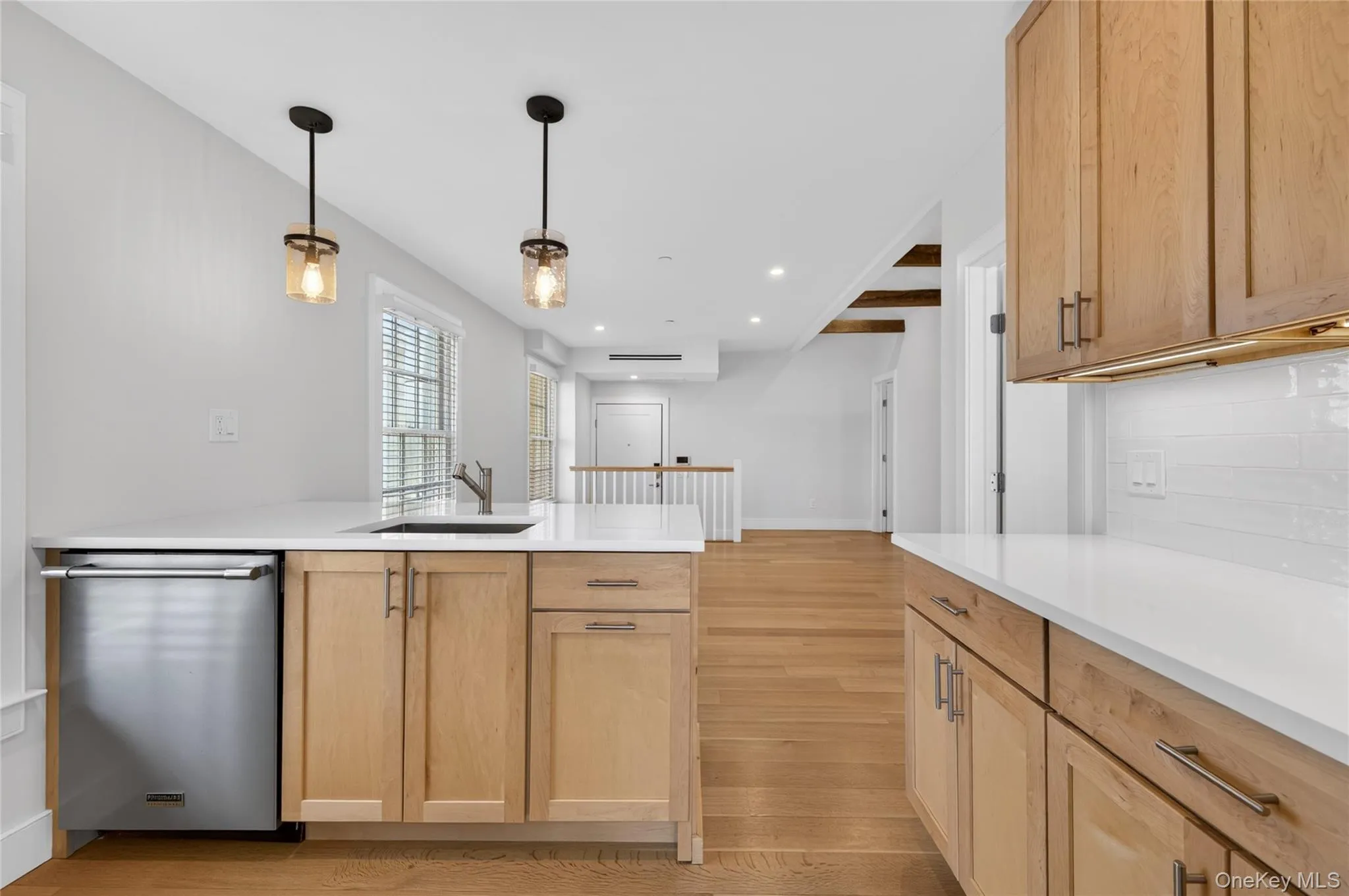 Kitchen featuring light wood cabinetry, white countertops, stainless steel dishwasher, undermount sink with a gooseneck faucet, and two pendant light fixtures Kitchen featuring light wood cabinetry, white countertops, stainless steel dishwasher, undermount sink with a gooseneck faucet, and two pendant light fixtures