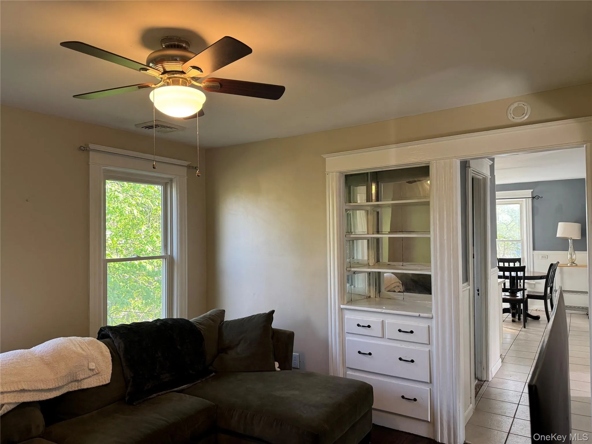Living area featuring a ceiling fan with integrated lighting, a built-in display cabinet with drawers, and a large window Living area featuring a ceiling fan with integrated lighting, a built-in display cabinet with drawers, and a large window