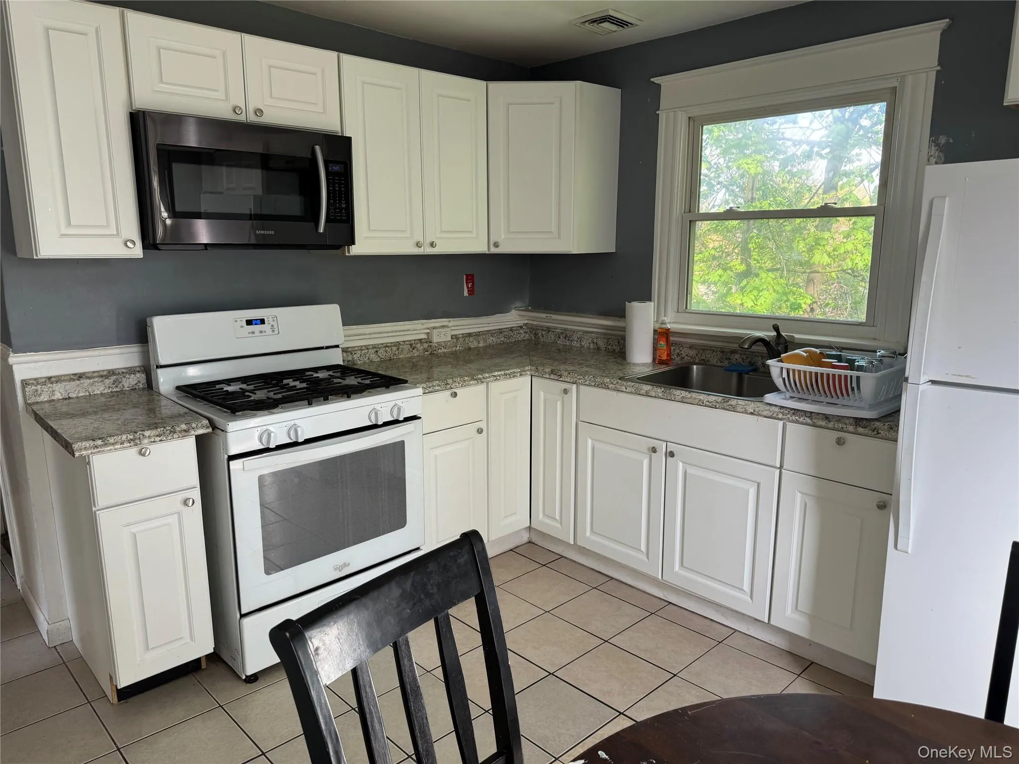 Kitchen featuring white cabinetry, light-toned countertops, tile flooring, a wall-mounted microwave, and a gas range Kitchen featuring white cabinetry, light-toned countertops, tile flooring, a wall-mounted microwave, and a gas range