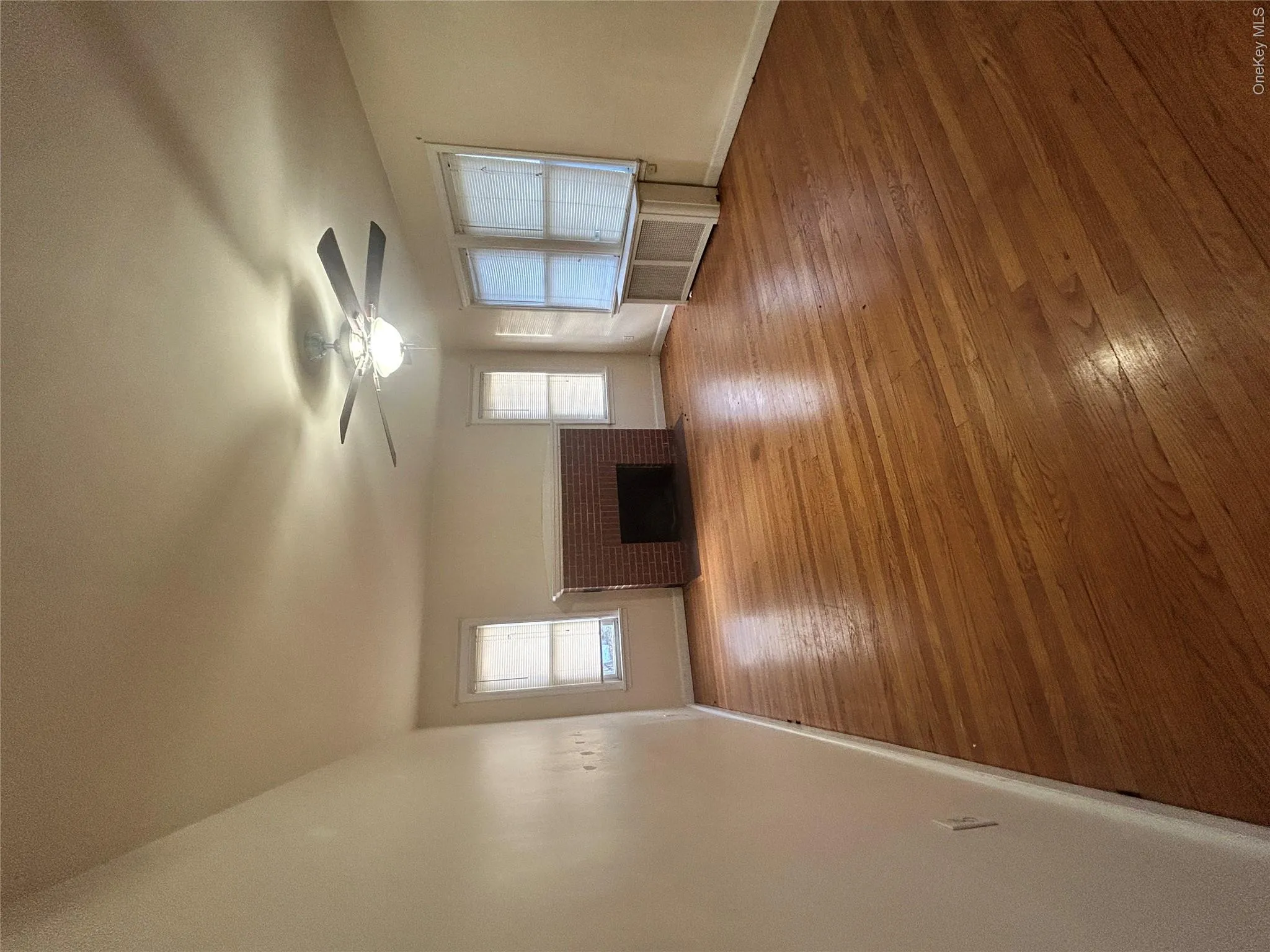 Unfurnished living room featuring hardwood / wood-style floors, a brick fireplace, radiator, and a ceiling fan Unfurnished living room featuring hardwood / wood-style floors, a brick fireplace, radiator, and a ceiling fan