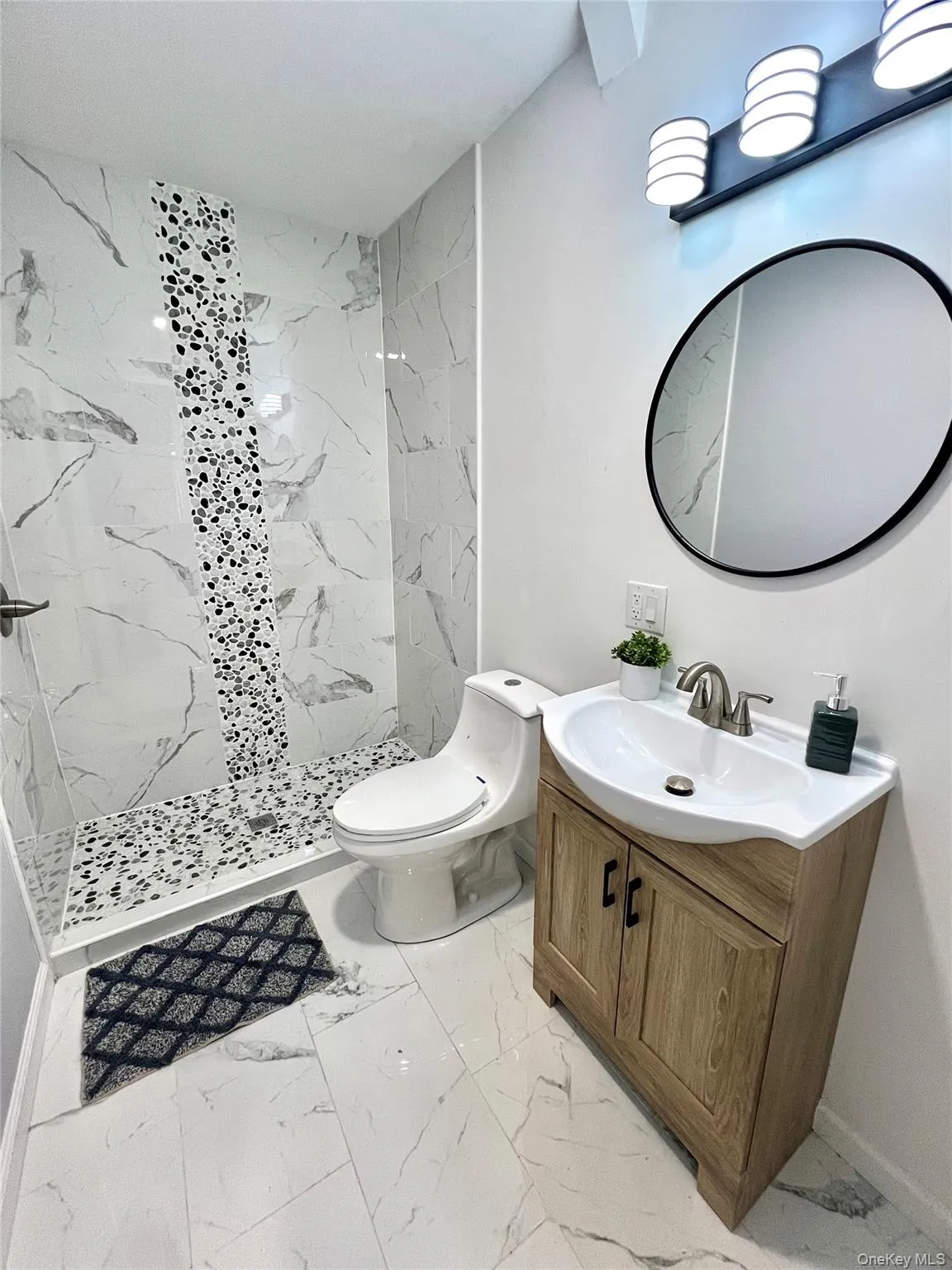 Full bath featuring a marble finish shower, vanity, and light marble finish flooring Full bath featuring a marble finish shower, vanity, and light marble finish flooring