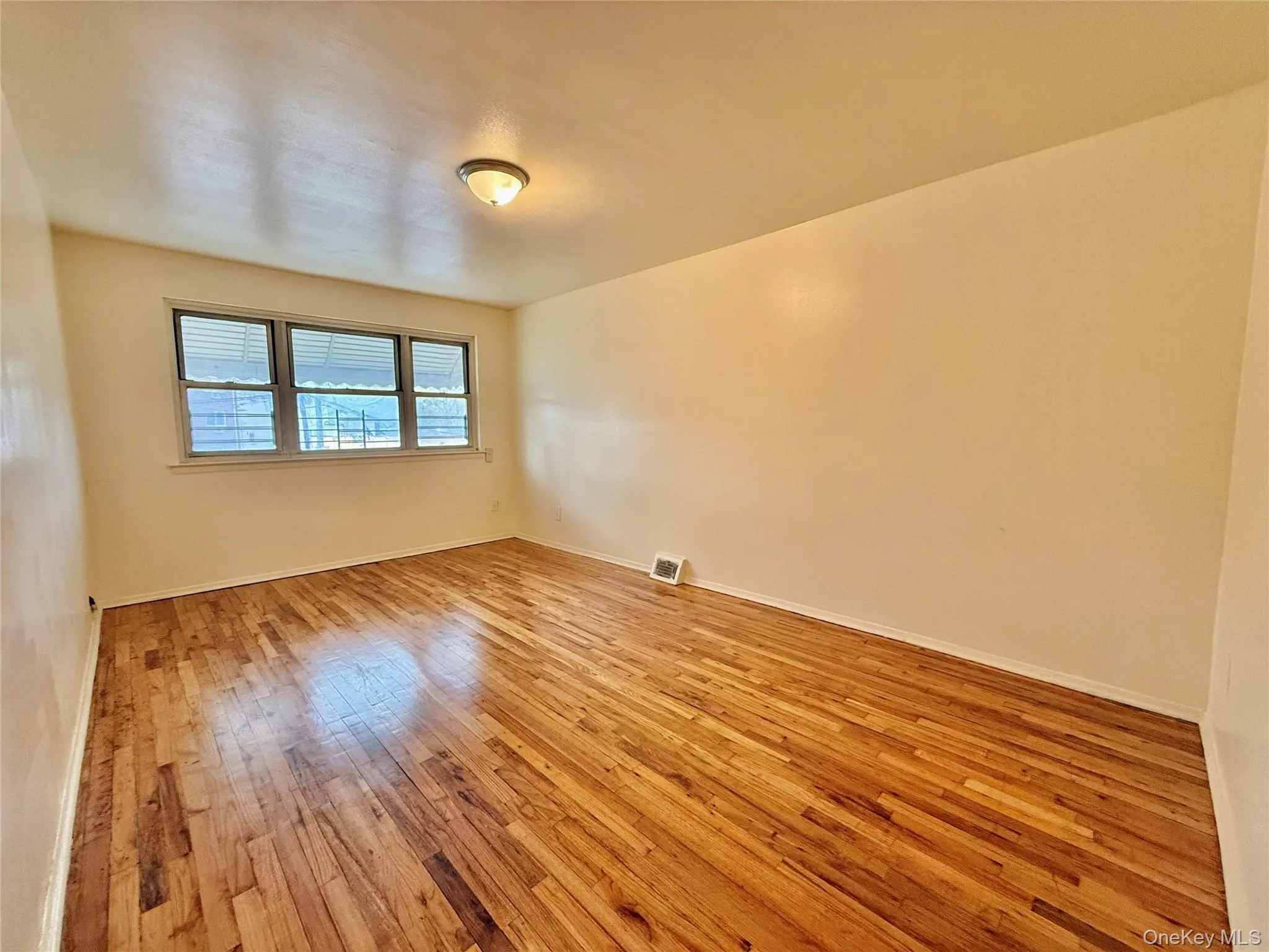 Hardwood flooring extends throughout this room, complemented by a multi-pane window with horizontal blinds and a flush-mount ceiling light fixture Hardwood flooring extends throughout this room, complemented by a multi-pane window with horizontal blinds and a flush-mount ceiling light fixture